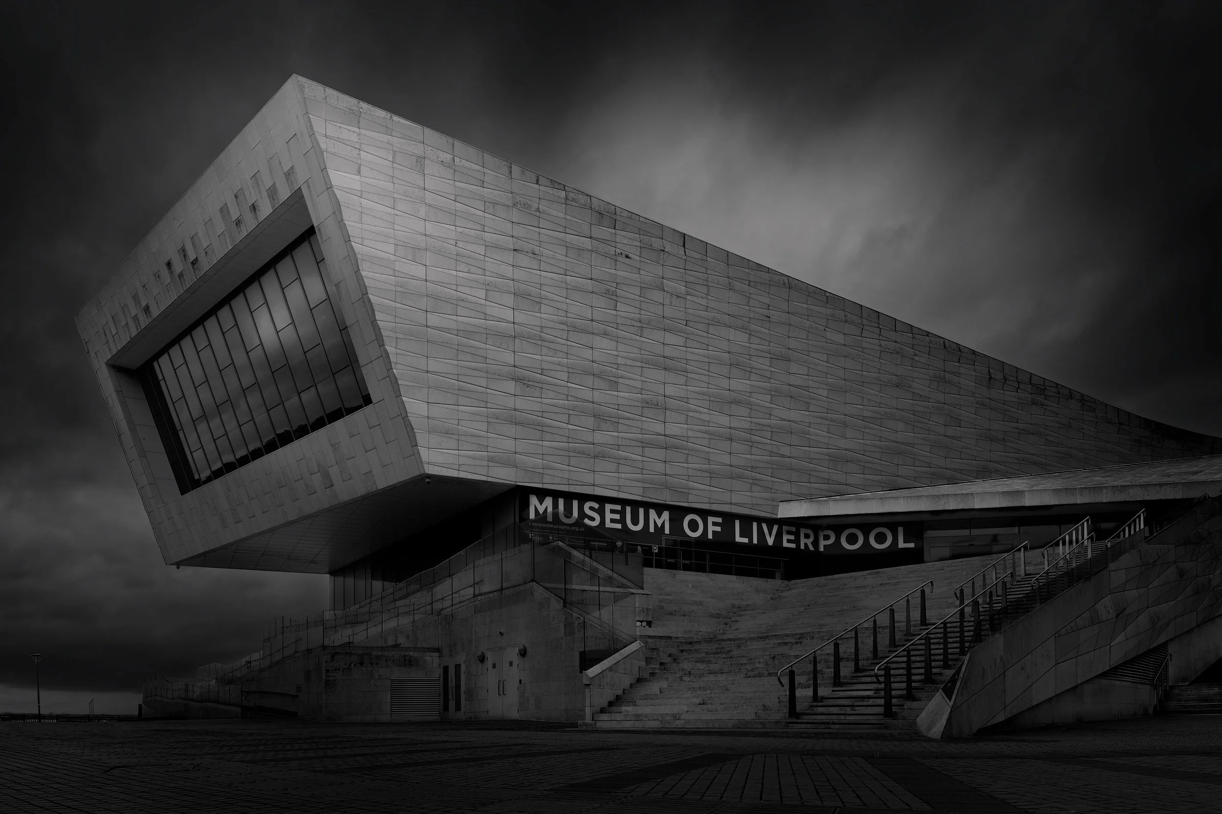 [architecture] [uk] [liverpool] [blackandwhite] Museum of Liverpool waterfront B&W with bold cantilevered limestone volume jutting over entrance steps. Architectural Photography by Jim Scott.