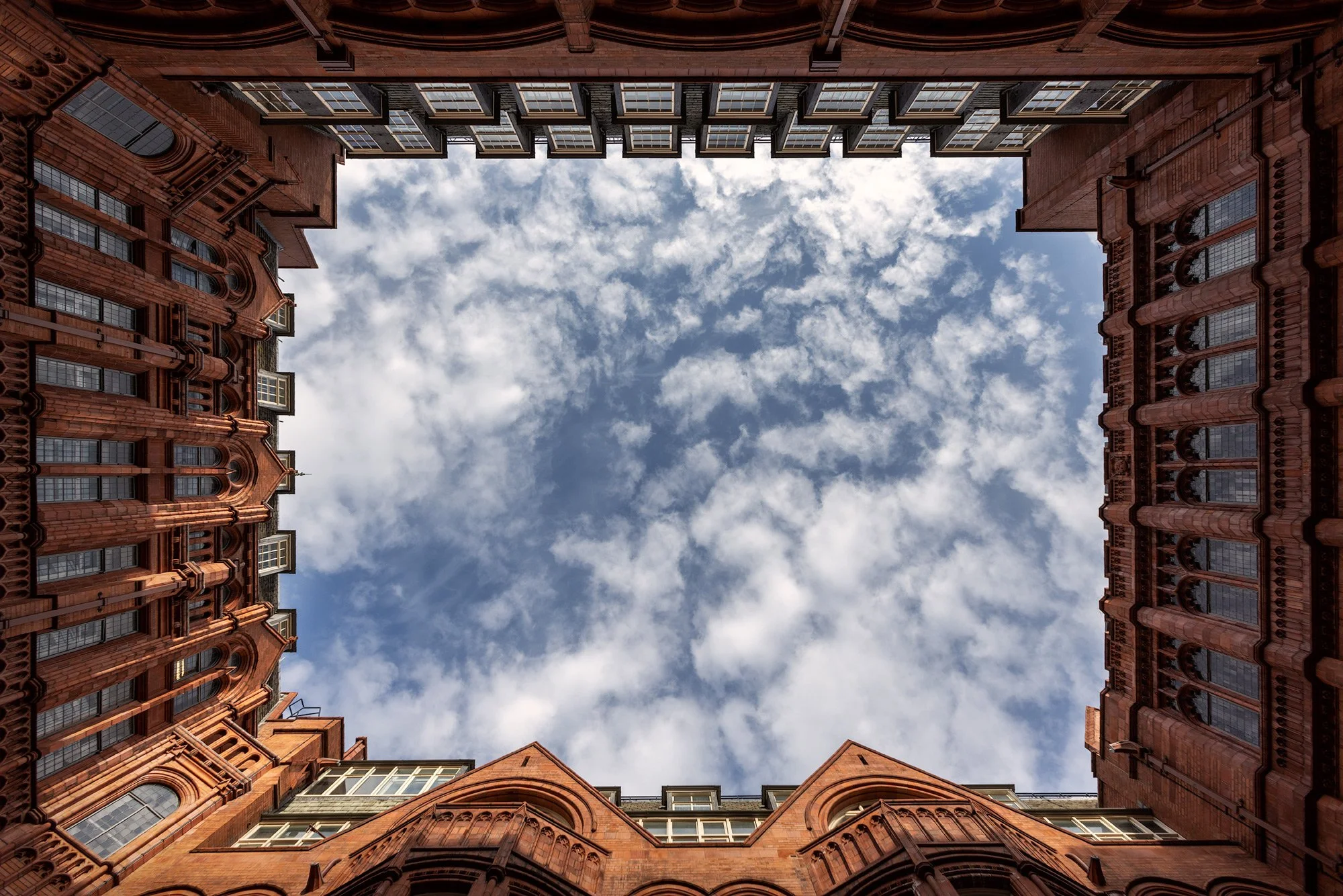 Victorian Gothic architecture in London: The internal courtyard of Waterhouse Square (Prudential Assurance Building) in Holborn. A stunning symmetrical upward perspective designed by Alfred Waterhouse, featuring ornate red terracotta brickwork framin