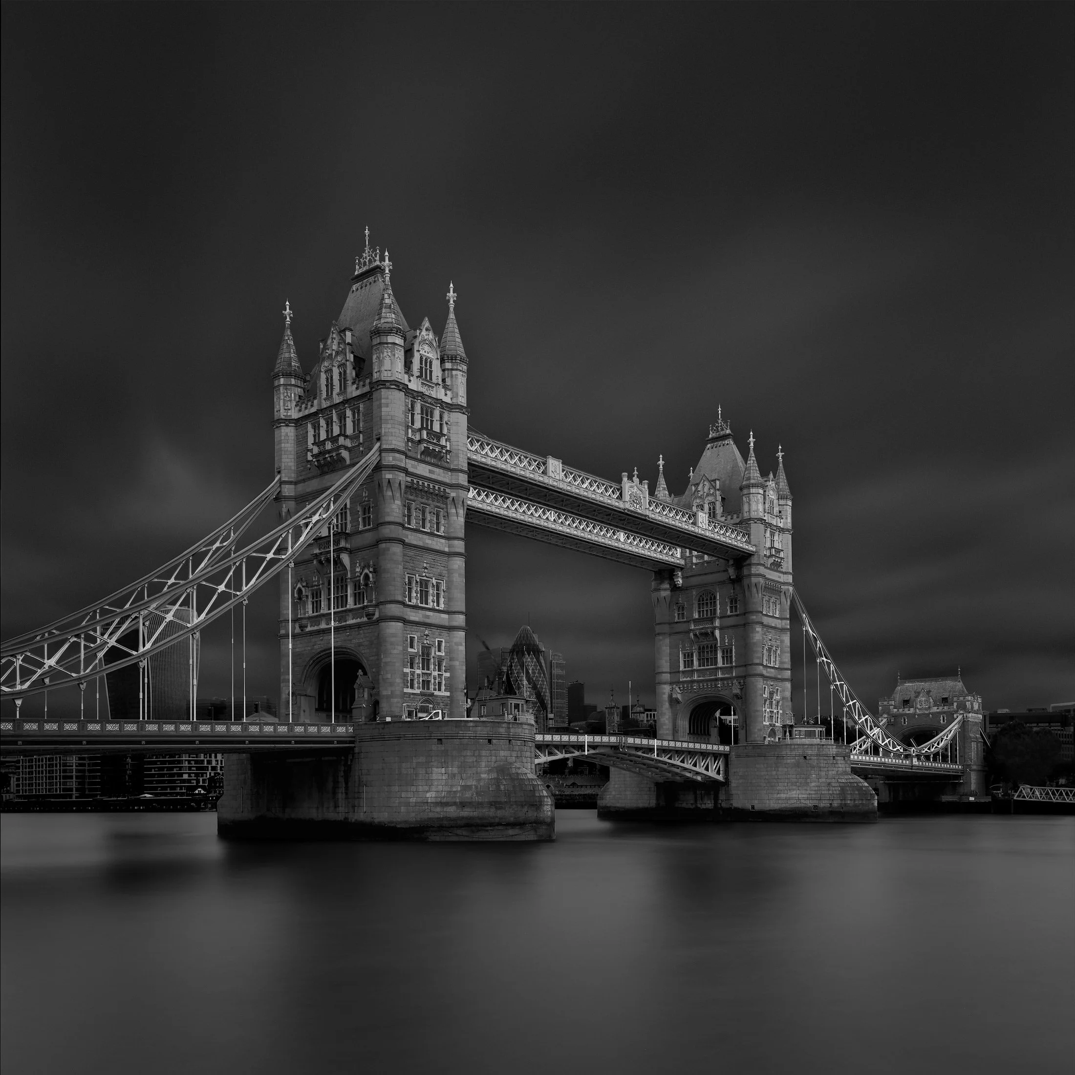 Victorian Gothic engineering in London, UK: A dramatic monochromatic long-exposure study of Tower Bridge over the River Thames. This architectural photograph captures the symmetrical grandeur of the bridge’s iconic towers and intricate suspension cab