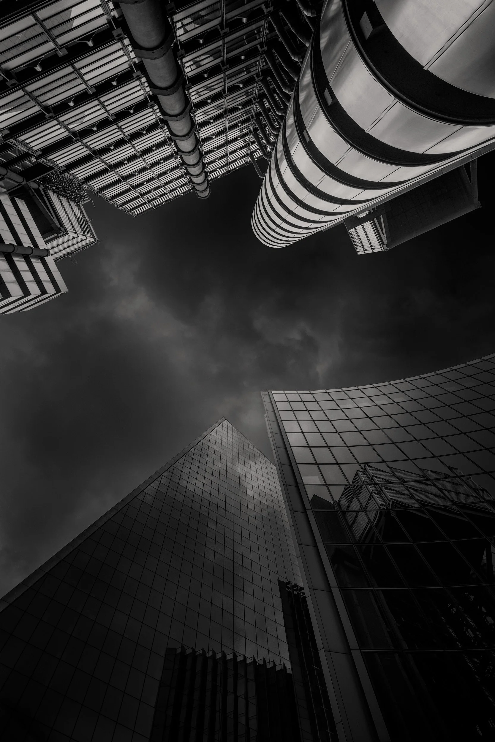 [architecture] [uk] [london] [blackandwhite] Lloyd's of London upward monochrome, Scalpel and Willis Towers converging above, exposed steel pods framing a dark sky. Architectural Photography by Jim Scott.