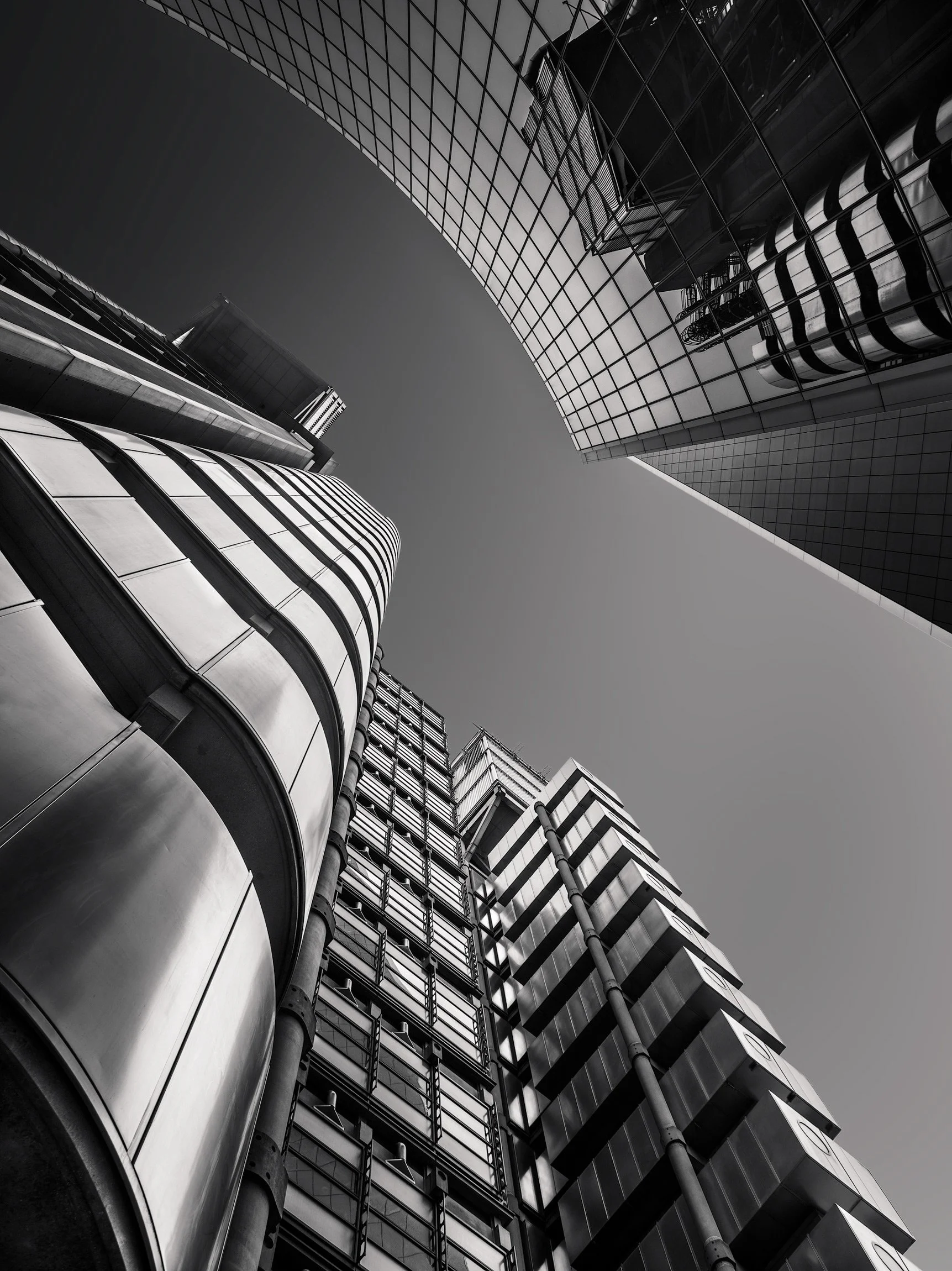 High-tech and commercial architecture in the City of London: A dramatic monochromatic study of the Lloyd's building and the Willis Building (51 Lime Street). This extreme upward perspective captures the sharp contrast between the industrial, "inside-