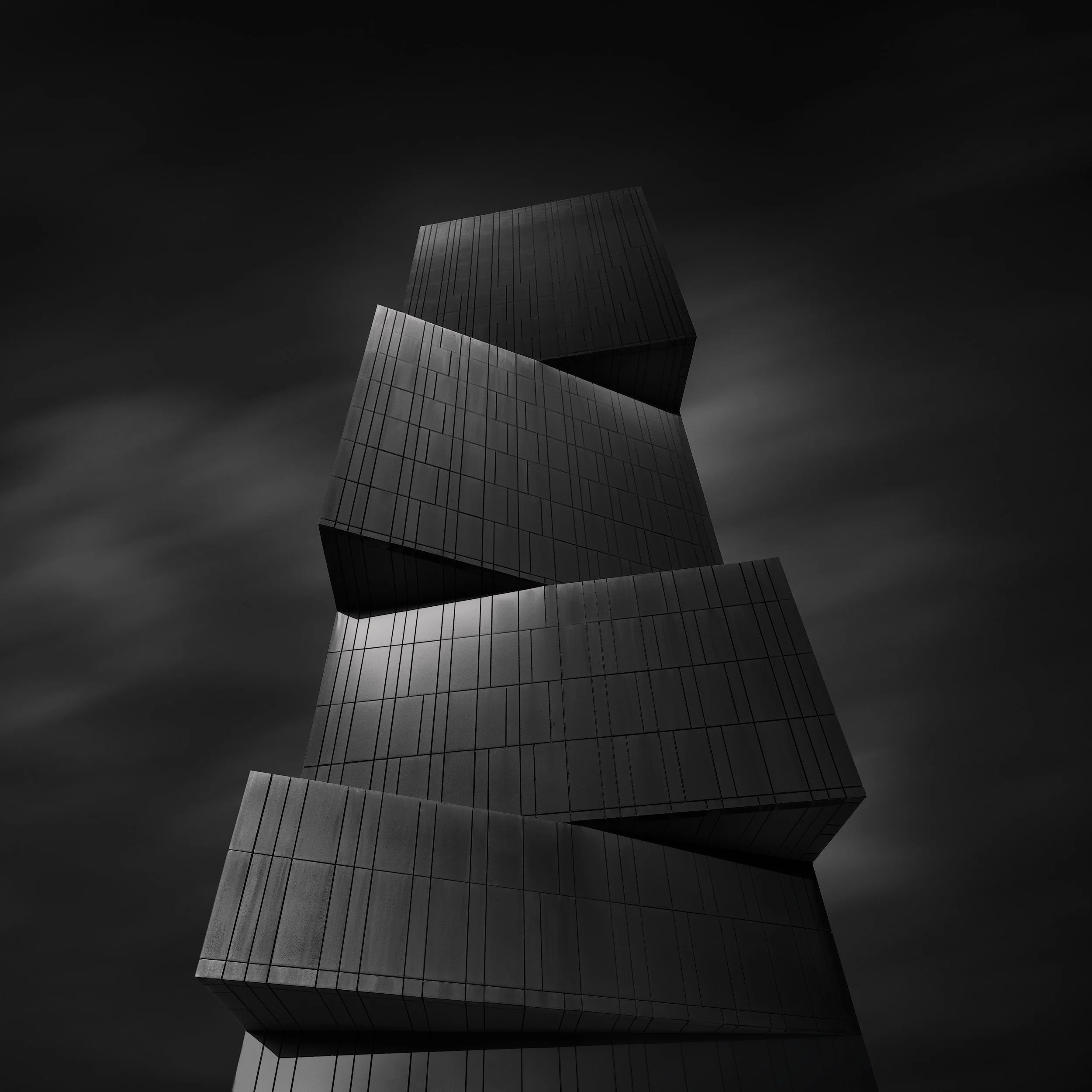 [architecture] [uk] [leeds] [blackandwhite] [square] Broadcasting Place Leeds monochrome upward study, four angular iron-clad cubes stacked and offset under a dramatic sky. Architectural Photography by Jim Scott.