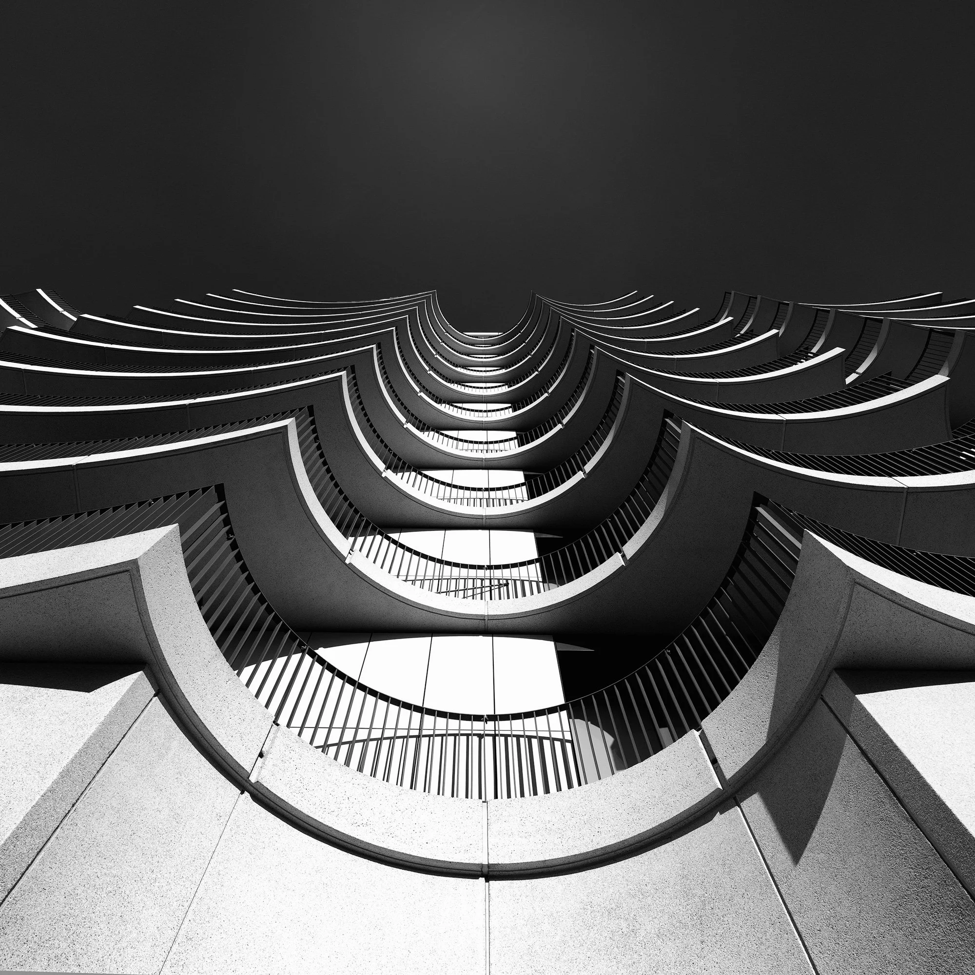 [architecture] [uk] [london] [blackandwhite] [square] Delphic House London, looking up through stacked repeating curved balconies forming hypnotic concentric arches, bold graphic composition. Architectural Photography by Jim Scott.