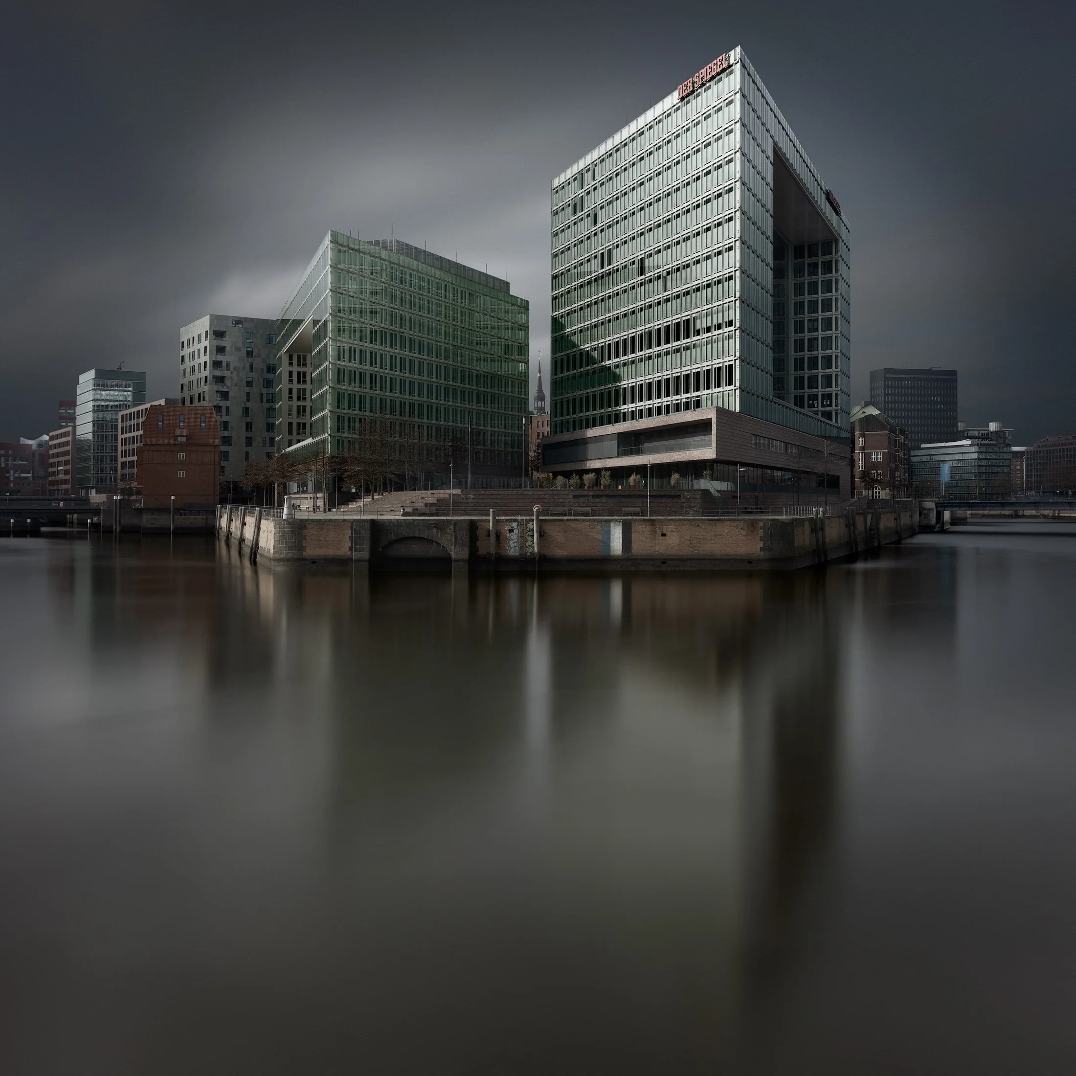 Contemporary media architecture in Hamburg, Germany: A striking monochromatic long exposure of the Spiegel Headquarters at Ericusspitze, designed by Henning Larsen Architects. The photograph features the building's iconic multi-story glass atrium and