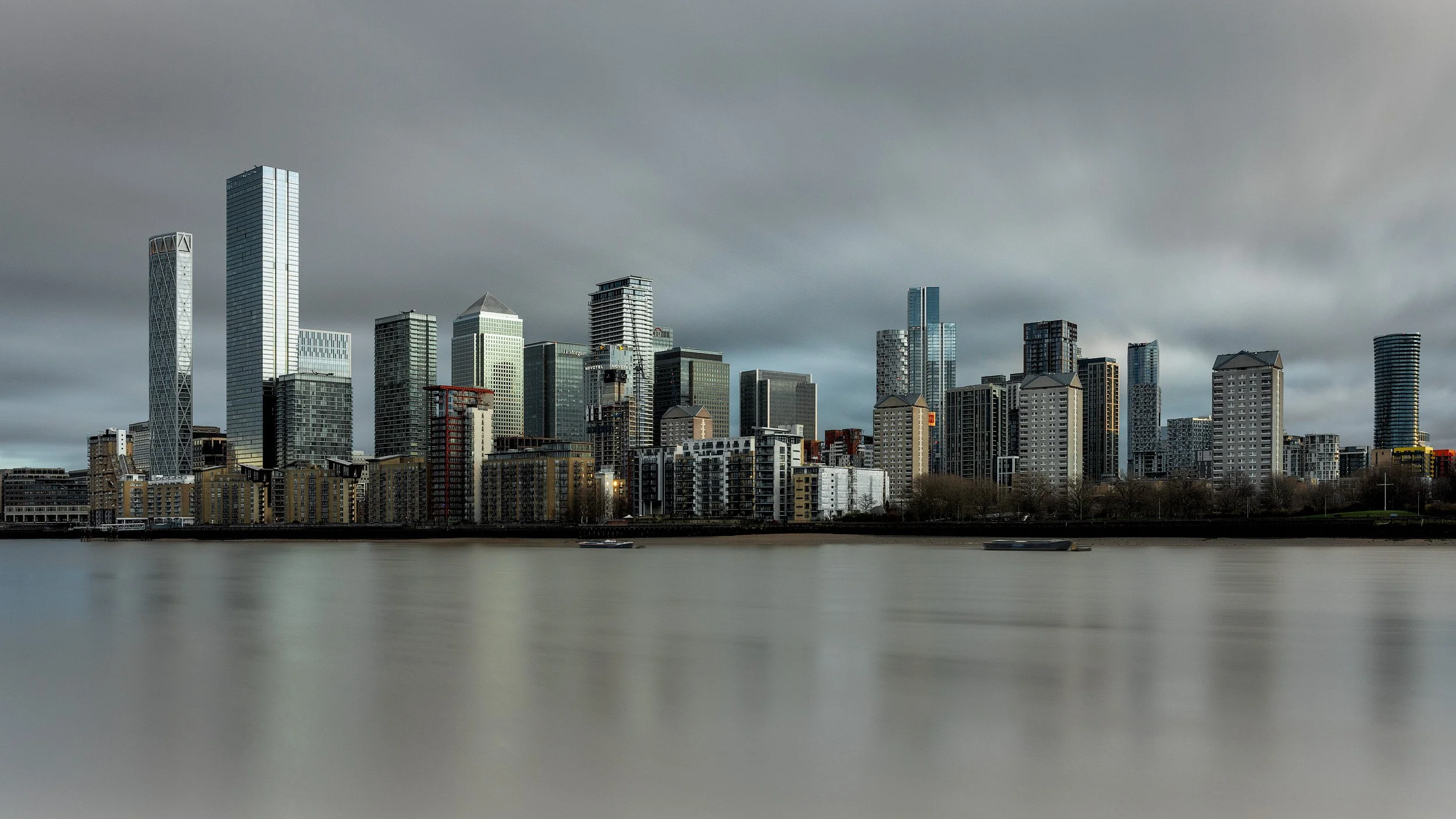Contemporary commercial and residential architecture in Canary Wharf, London: A dramatic study of the Docklands skyline from across the River Thames. This panoramic architectural photograph captures the towering crystalline form of the Landmark Pinna