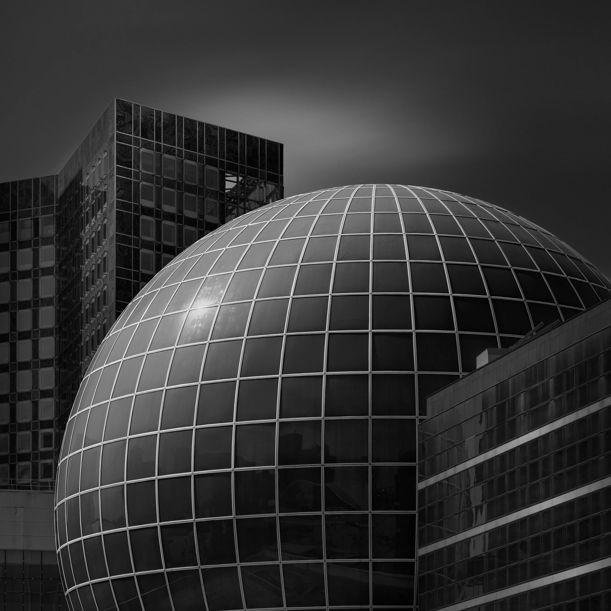 [architecture] [europe] [paris] [blackandwhite] [square] Tour Pascal La Défense Paris, glass geodesic dome sitting centrally between two flanking slab tower blocks under dark Architectural Photography by Jim Scott.