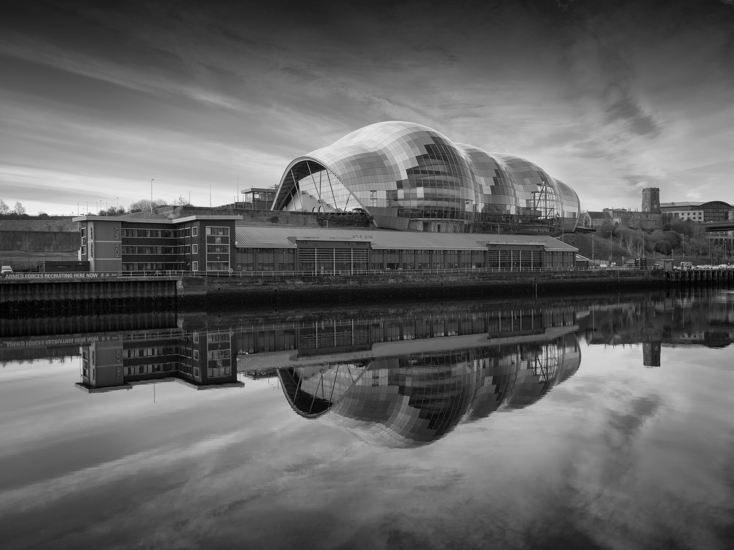 [architecture] [uk] [gateshead] [blackandwhite] Sage Gateshead glass shell concert hall reflected in River Tyne, sweeping curved roofline, black and white monochrome. Architectural Photography by Jim Scott.