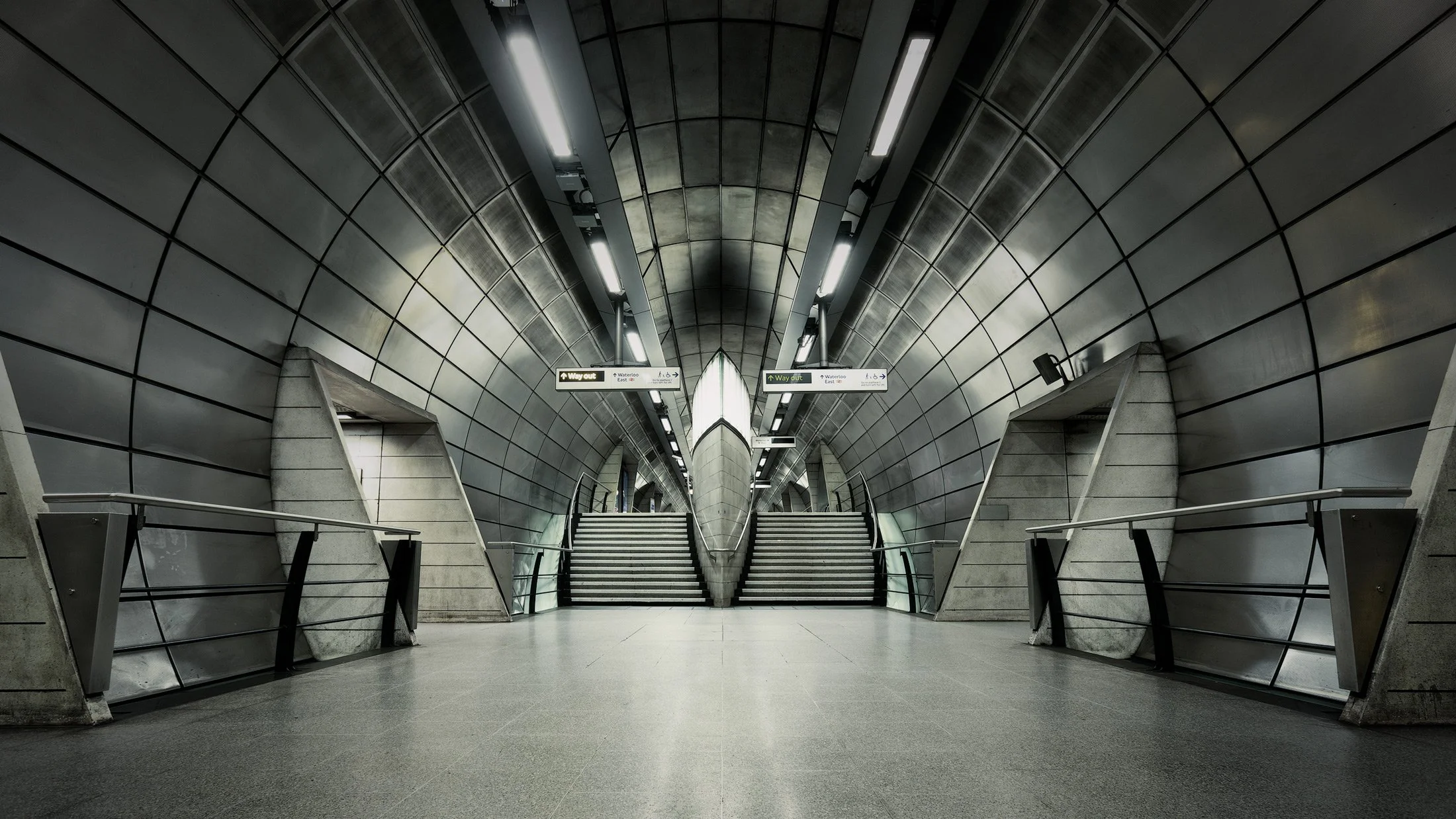 Sovereign high-tech transit design in London, UK: A symmetrical interior study of Southwark Underground Station, designed by MacCormac Jamieson Prichard. This architectural photograph captures the rhythmic precision of the stainless steel tunnel and 