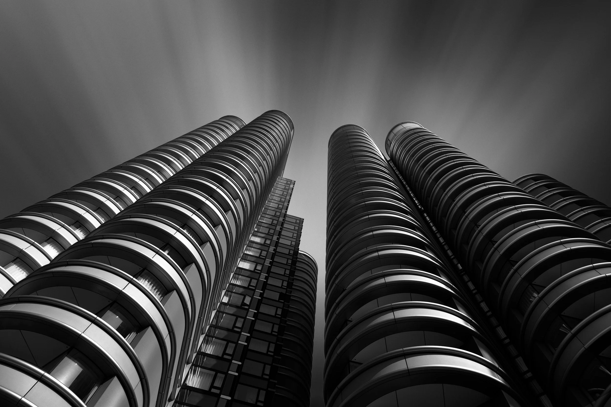 Contemporary residential architecture on the Albert Embankment, London: A dramatic monochromatic study of The Corniche, designed by Foster + Partners. This low-angle architectural photograph captures the rhythmic, curved balconies and the smooth cyli