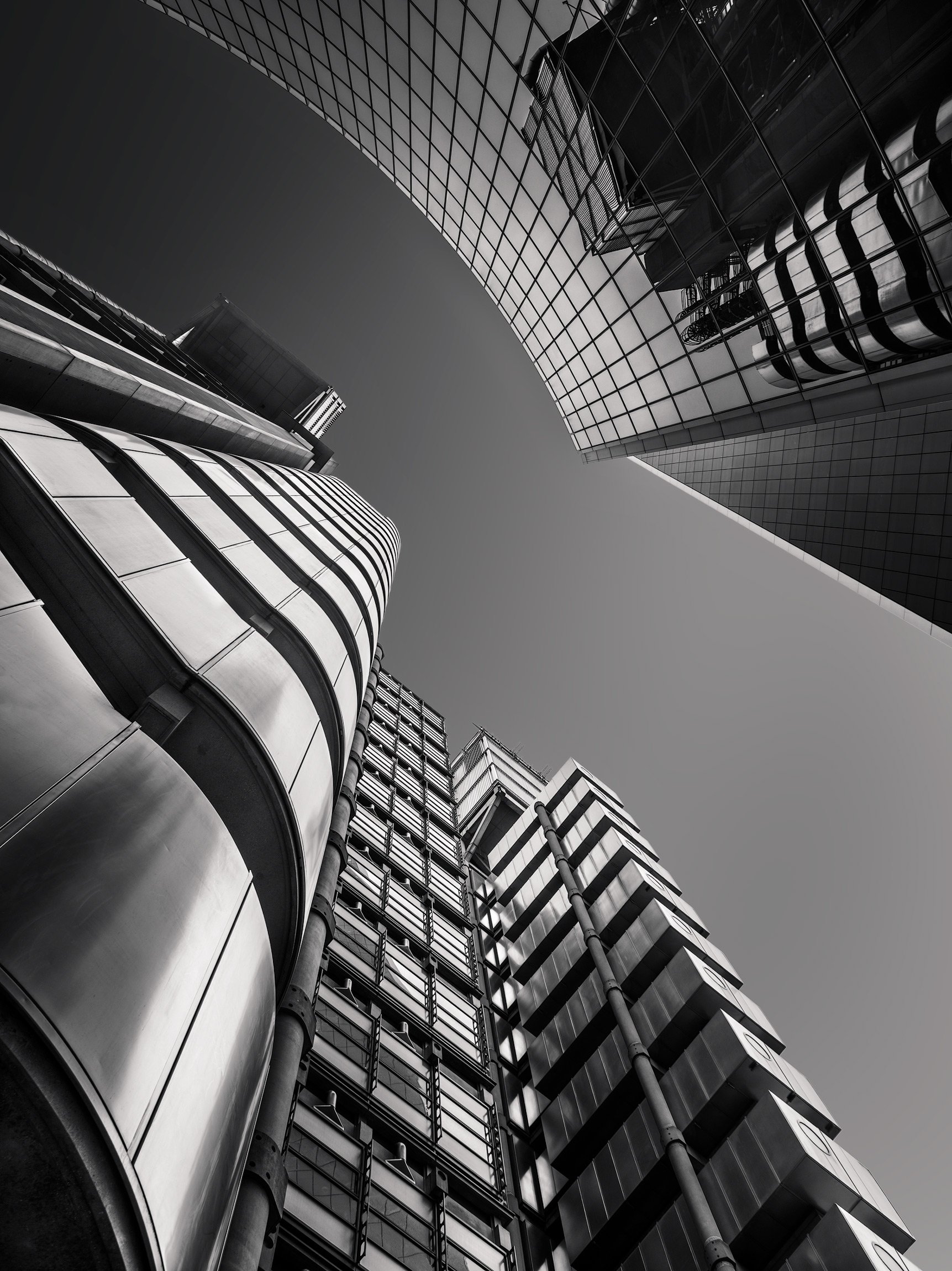 [architecture] [uk] [london] [blackandwhite] Lloyd's of London and Willis Building, looking up between high-tech steel and curved glass towers, bold black and white. Architectural Photography by Jim Scott. 
