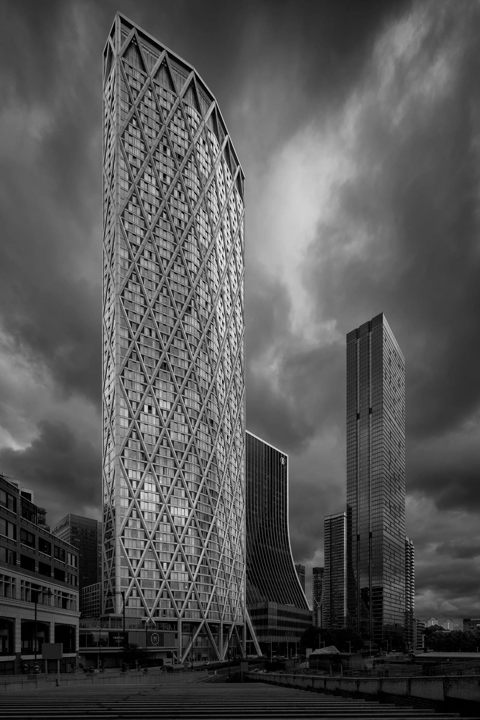 [architecture] [uk] [london] [blackandwhite] Newfoundland tower Canary Wharf monochrome, diamond-lattice diagrid rising amid older stone and glass neighbours. Architectural Photography by Jim Scott.
