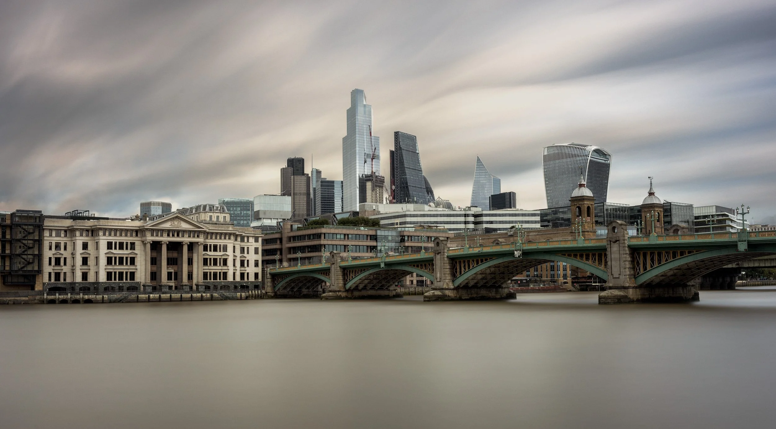 London City architecture: Vintners’ Place and the historic Vintners’ Hall at Southwark Bridge. A colour architectural photograph featuring the classical 1990s postmodern facade and the riverfront pillars of the 17th-century livery hall, set against t