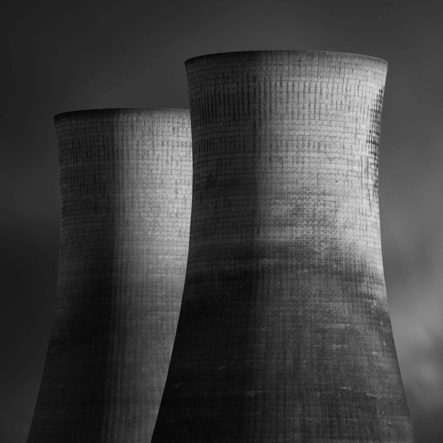 [architecture] [uk] [middlesbrough] [blackandwhite] [square] Two textured concrete cooling towers rise at a chemical plant in Haverton Hill, Teesside, against a plain grey sky. Architectural Photography by Jim Scott