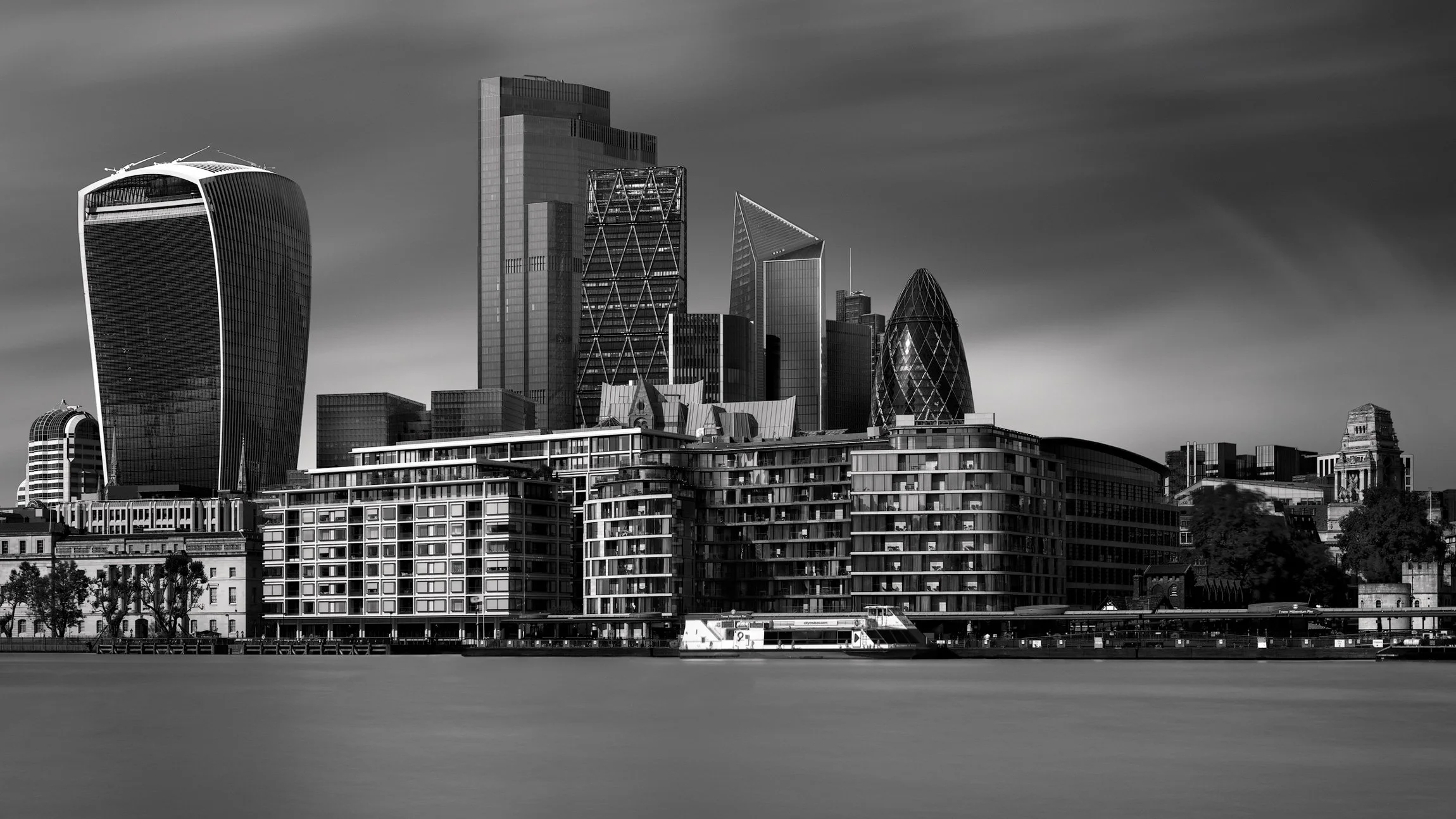 [architecture] [uk] [london] [blackandwhite] [panoramic] City of London skyline B&W long exposure across the Thames, Walkie Talkie, Gherkin and Scalpel under a streaked sky. Architectural Photography by Jim Scott.