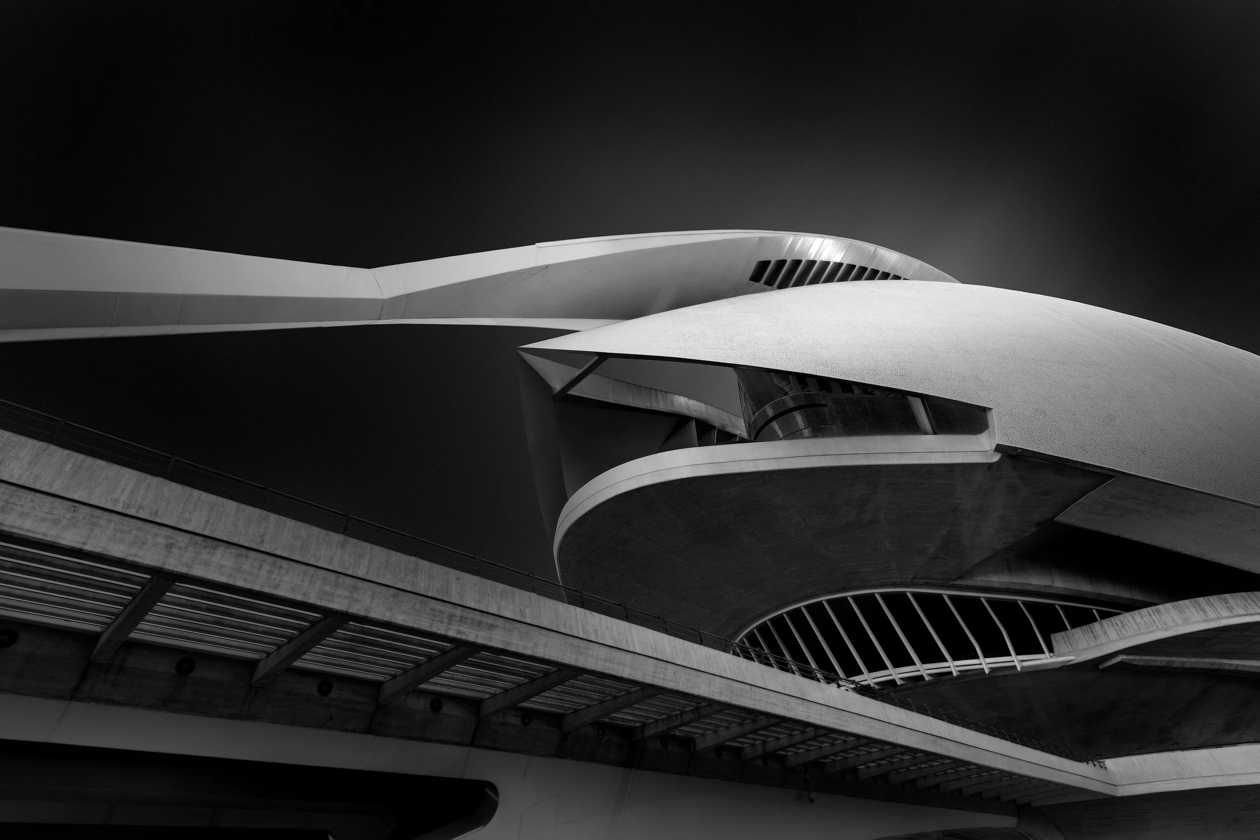 Neo-futurist architecture in Valencia, Spain: A dramatic monochromatic study of the Palau de les Arts Reina Sofía, designed by Santiago Calatrava. This architectural photograph highlights the soaring, aerodynamic shell and the complex interplay of cu