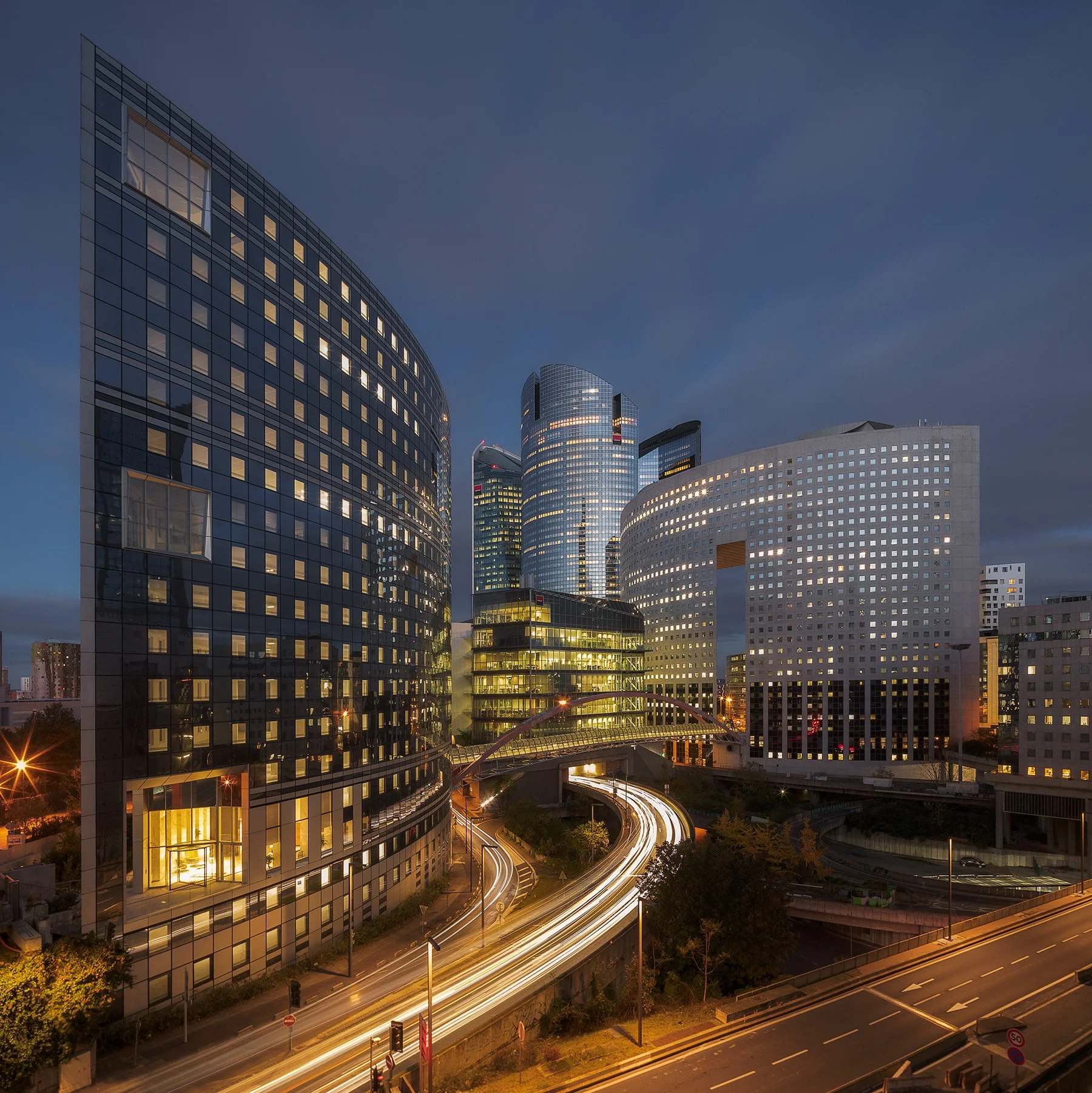 Contemporary urban architecture in La Défense, Paris: A vibrant blue-hour study of the French financial district. This elevated cityscape photograph captures the curved glass facades of Tour Eqho and the iconic windowed silhouette of the Hôtel Meliá,