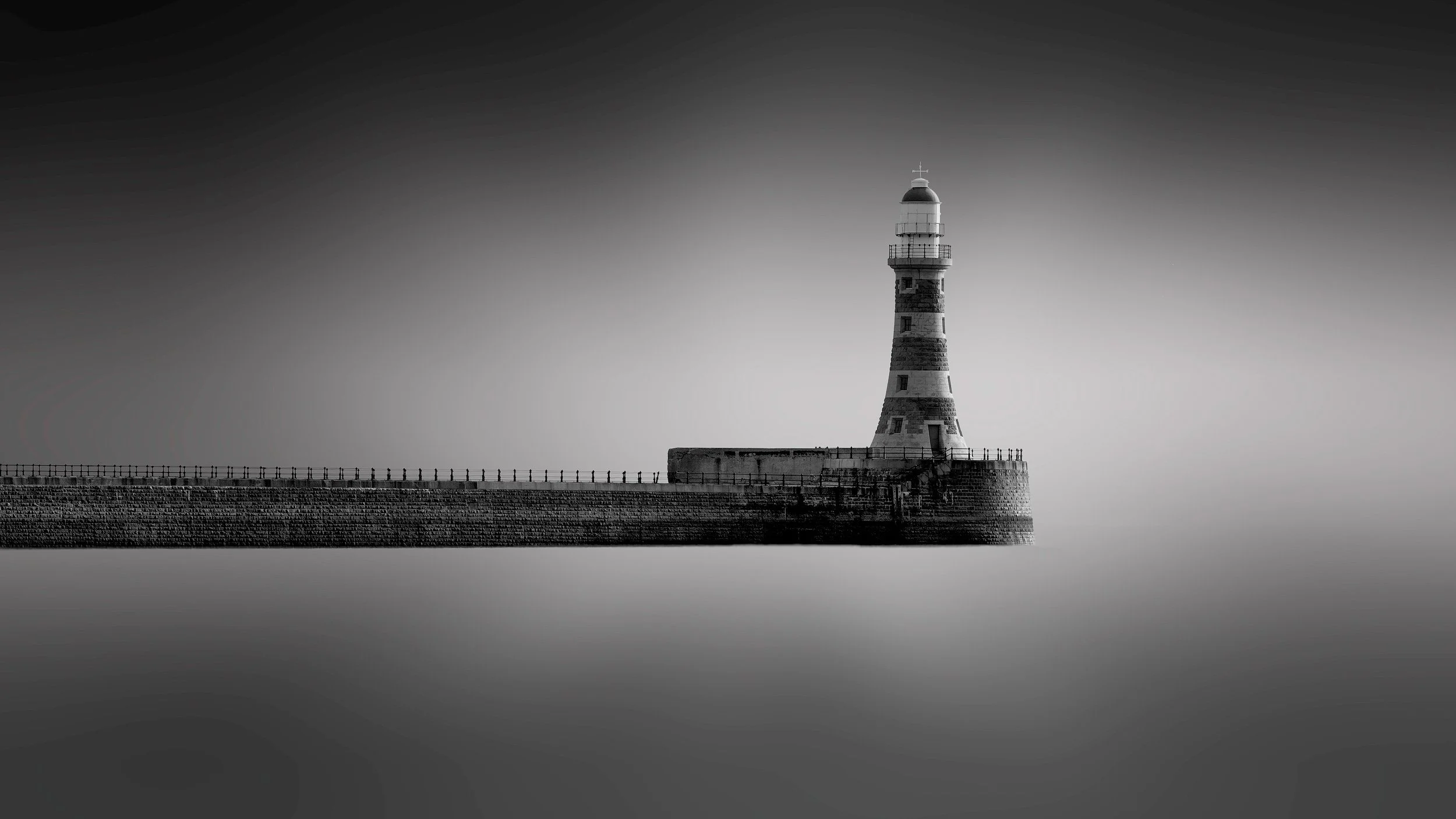 [architecture] [uk] [sunderland] [blackandwhite] [panoramic] Roker Pier Lighthouse Sunderland minimalist B&W, striped stone tower isolated at the pier end above a still sea. Architectural Photography by Jim Scott.