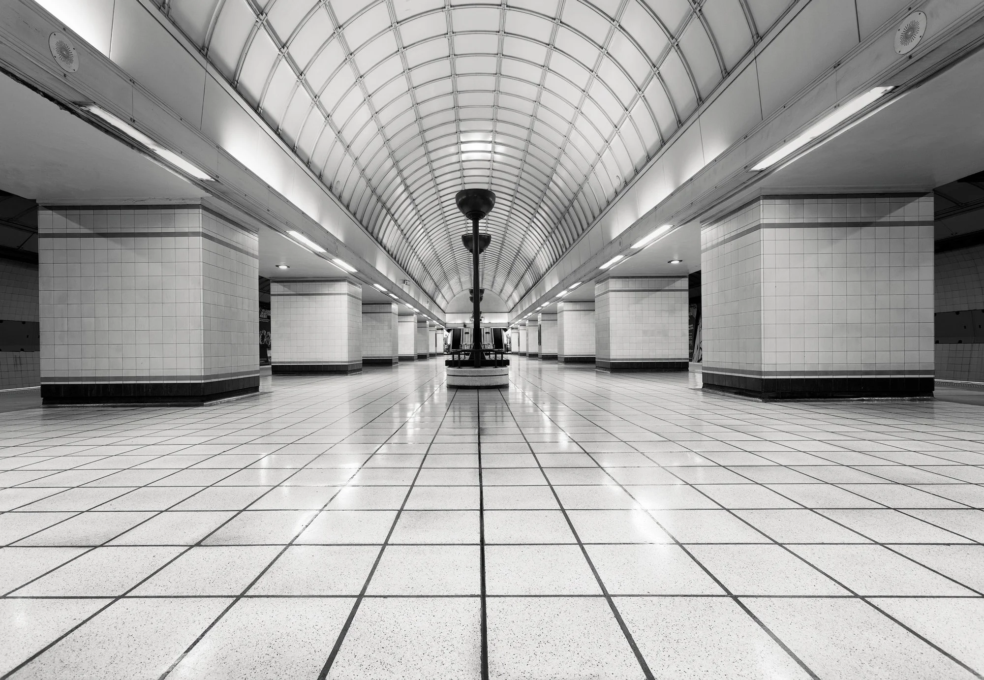 Modernist transport architecture in Ilford, London: A minimalist monochromatic study of Gants Hill Underground Station, designed by Charles Holden. This architectural photograph captures the vast, symmetrical concourse of the "Moscow Hall," featuring