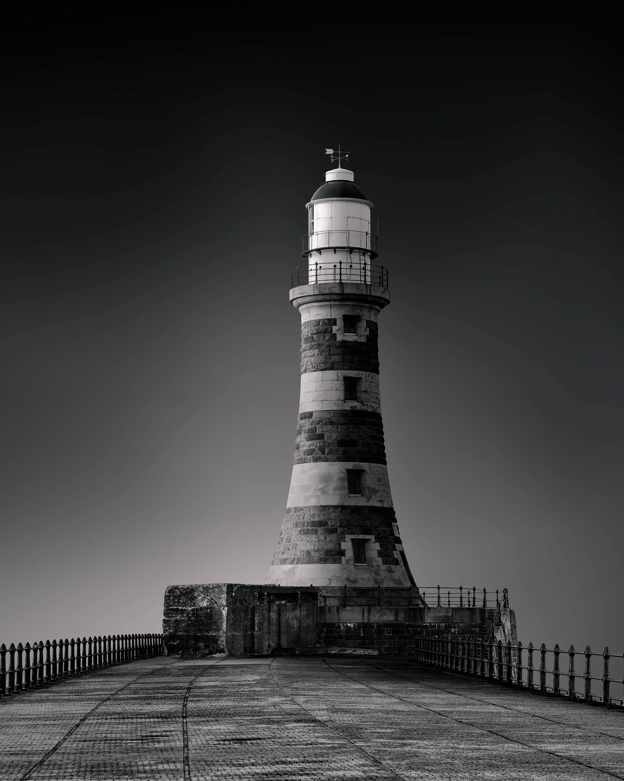 [architecture] [uk] [sunderland] [blackandwhite] Roker Lighthouse Sunderland from the pier, broad banded granite tower and dark lantern room against a graduated grey Architectural Photography by Jim Scott.