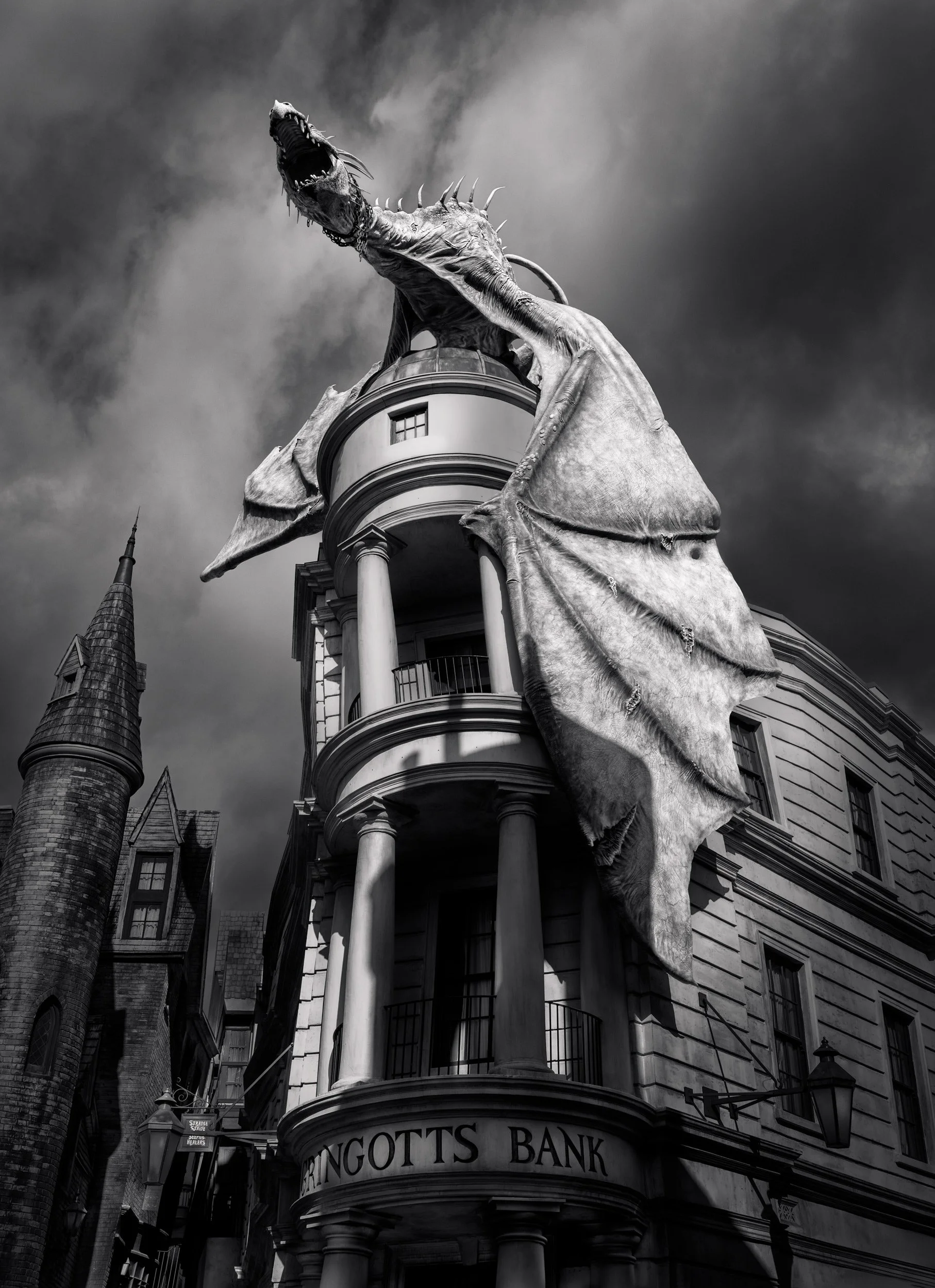 Themed neoclassical architecture at Universal Orlando: A dramatic monochromatic study of Gringotts Wizarding Bank. This low-angle photograph captures the imposing Ukrainian Ironbelly dragon atop the bank’s skewed columns and dome. The high-contrast b