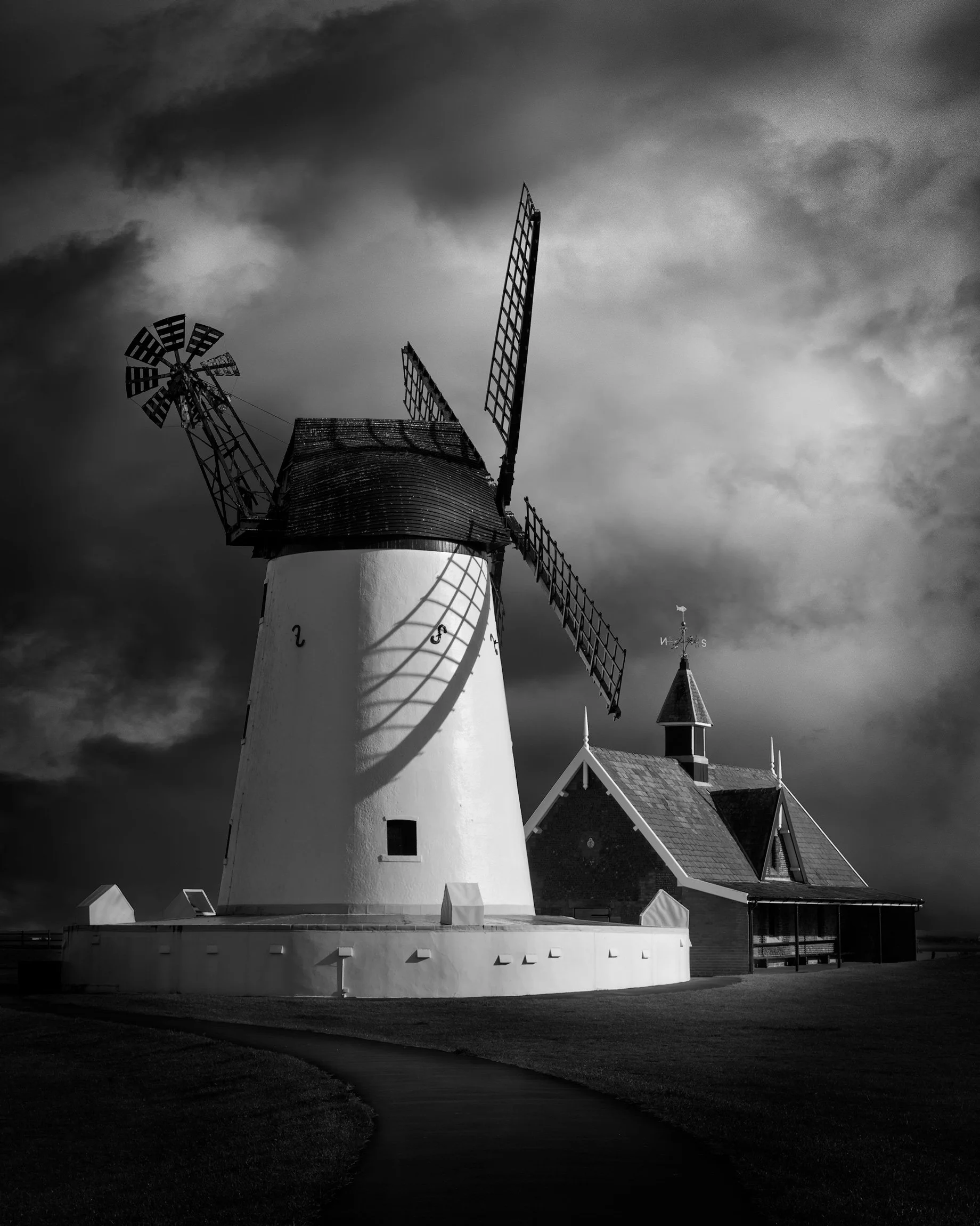 Historic maritime heritage in Lancashire, England: A dramatic monochrome study of the Lytham Windmill on the Fylde coast. This high-contrast architectural photograph captures the iconic 19th-century tower mill and lifeboat house against an atmospheri