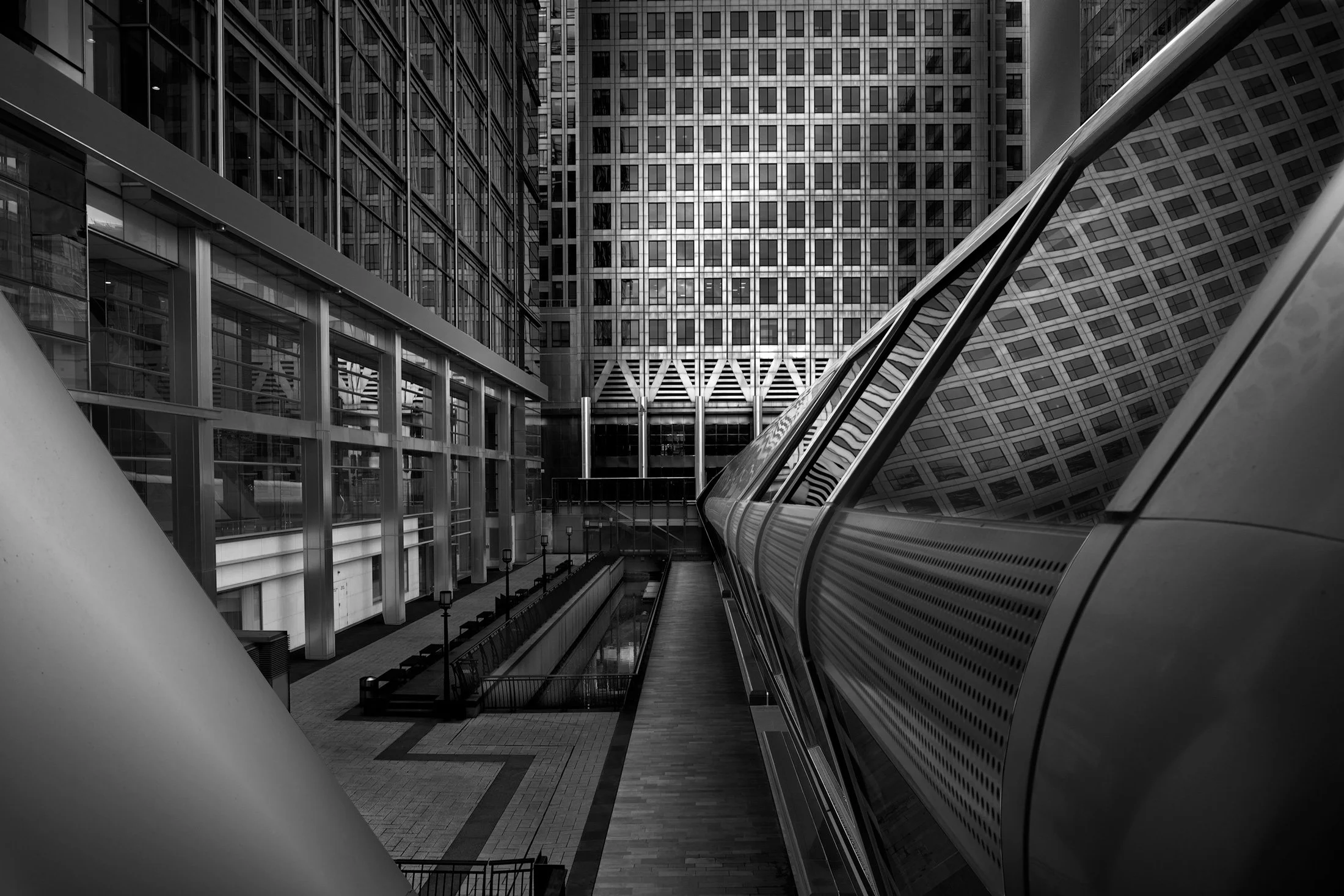 Modernist transit architecture in Canary Wharf, London: A black and white study from Adams Place featuring the futuristic bridge and Elizabeth Line station designed by Foster + Partners. This architectural photograph captures the complex interplay of