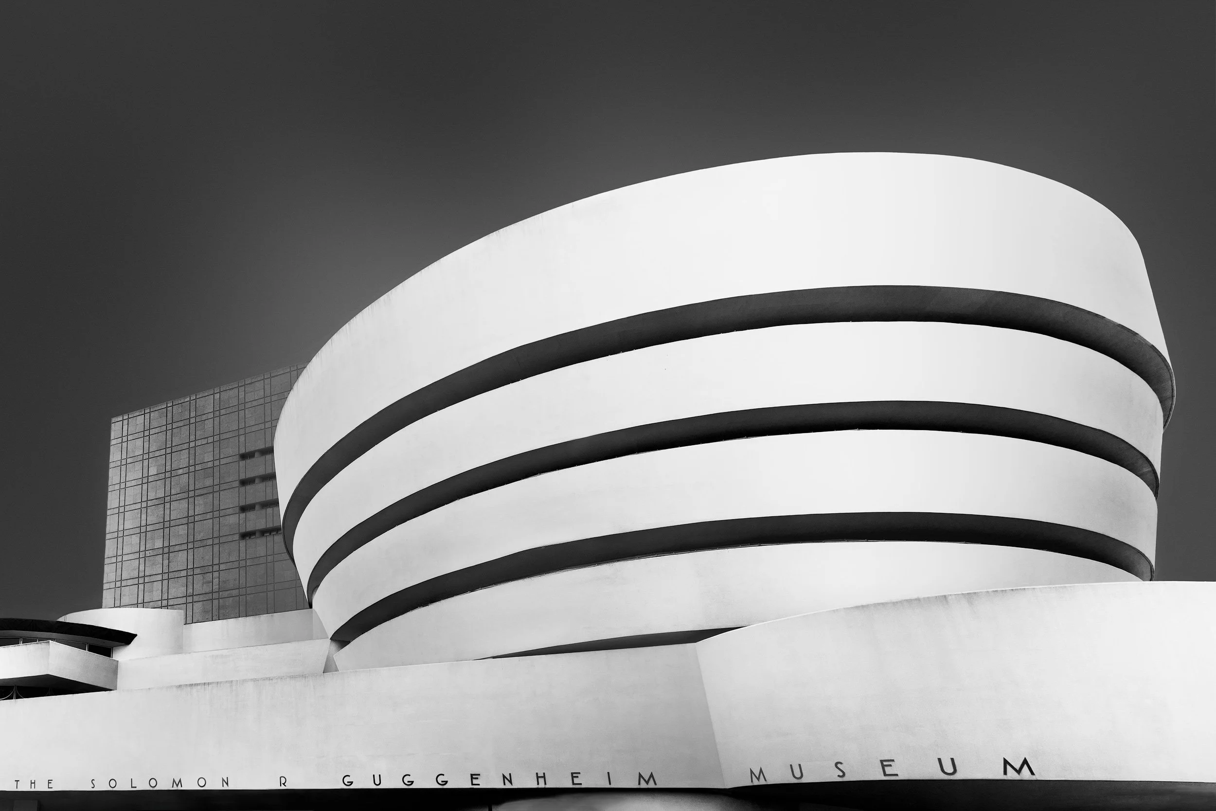Modernist architecture in New York City: The Solomon R. Guggenheim Museum designed by Frank Lloyd Wright. A clean black and white architectural photograph of the iconic white spiral rotunda and tiered concrete facade against a clear, dark sky on Manh