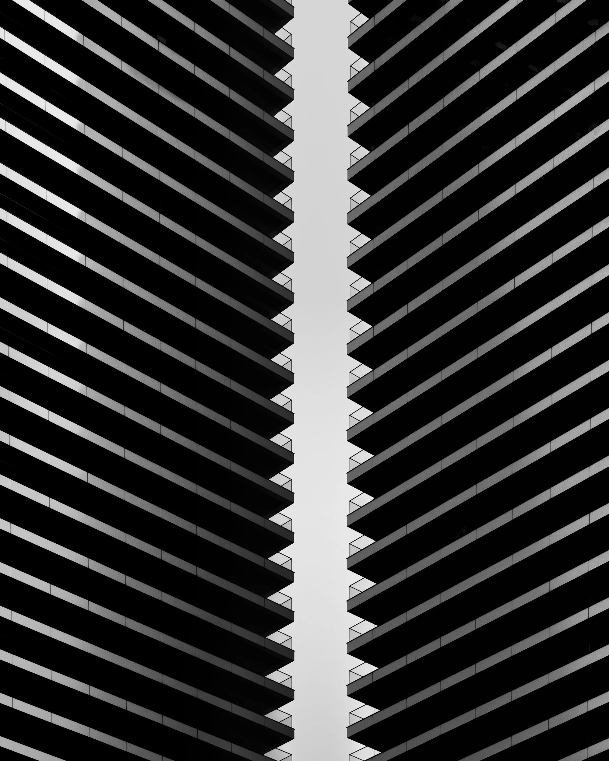 [architecture] [uk] [london] [blackandwhite] Wardian Canary Wharf London B&W, two mirrored towers with sawtooth diagonal balcony stacks split by a pale sky gap. Architectural Photography by Jim Scott.
