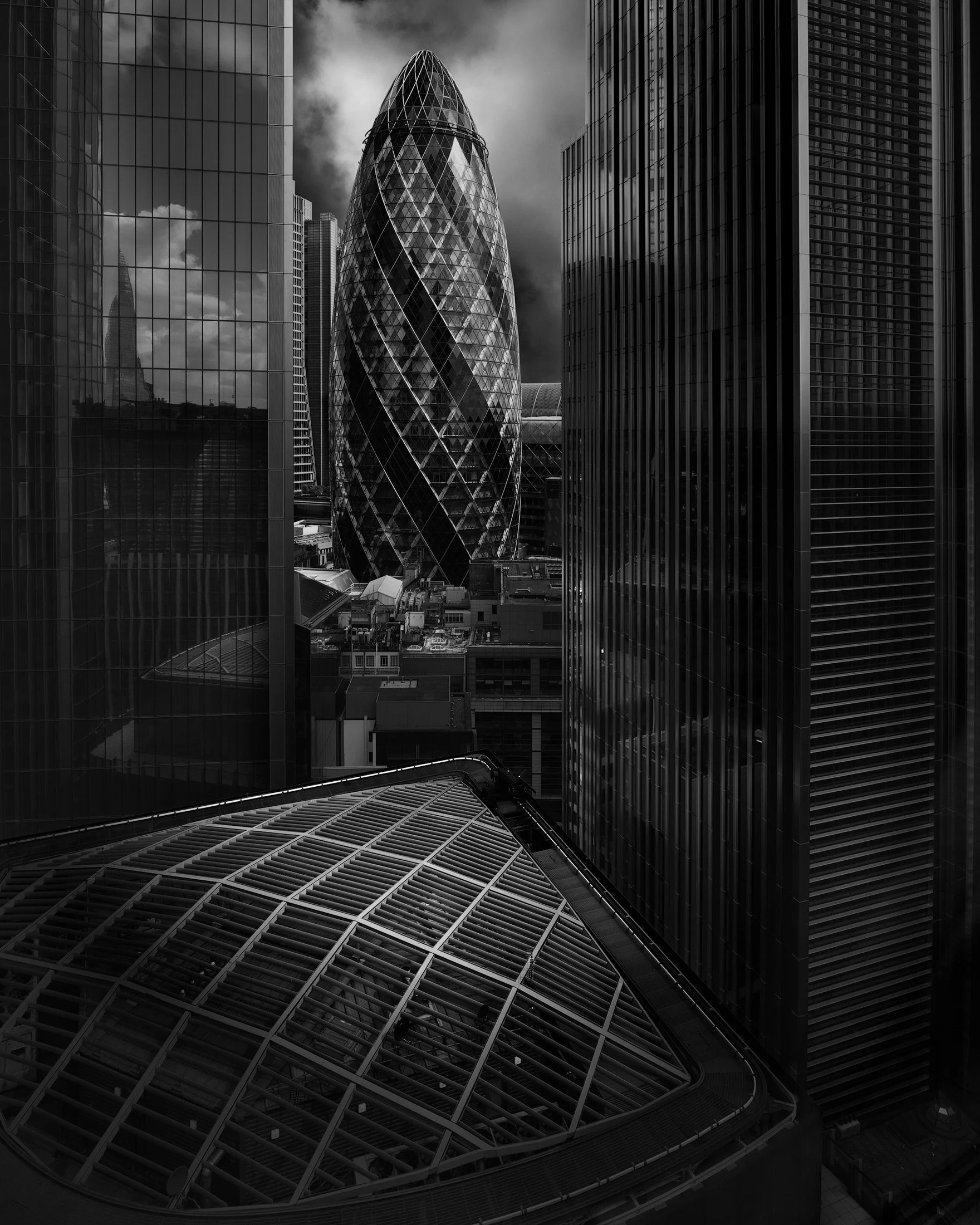 Contemporary skyscraper architecture in the City of London: A dramatic monochromatic study of 30 St Mary Axe (The Gherkin), designed by Foster + Partners seen from the roof-top garden at 120 Fenchurch Street. This high-angle rooftop photograph captur