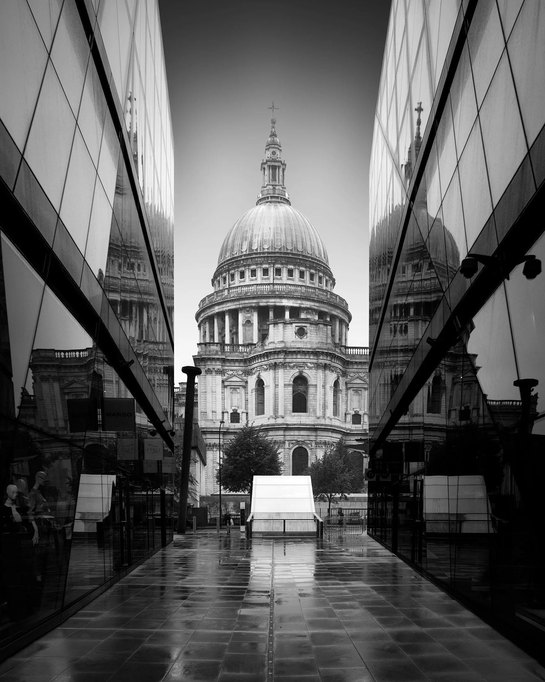 [architecture] [uk] [london] [blackandwhite] St Paul's Cathedral from One New Change London, Baroque dome framed between mirrored glass facades on a wet street. Architectural Photography by Jim Scott.
