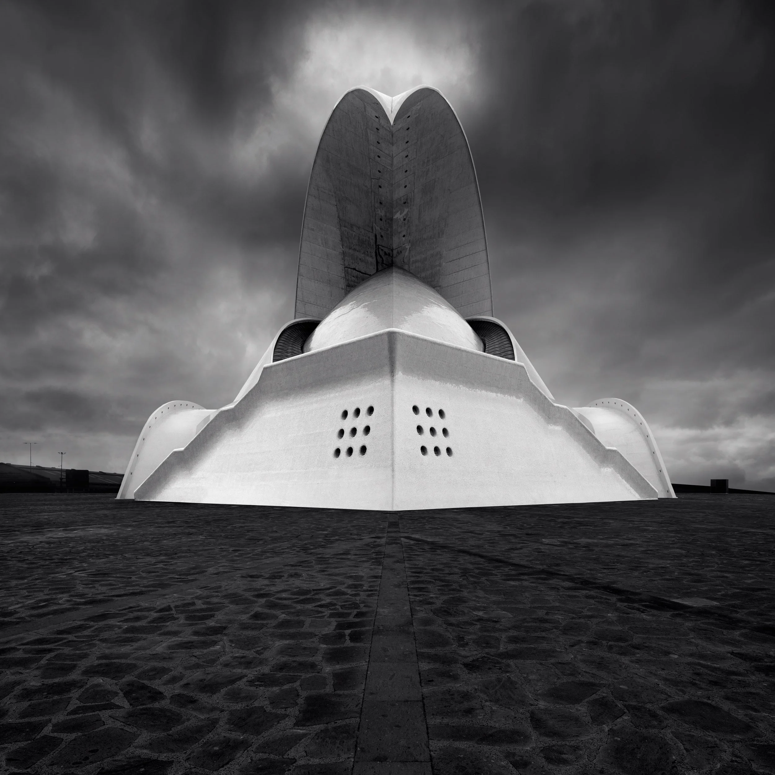 [architecture] [europe] [santacruzdetenerife] [blackandwhite] [square] Auditorio de Tenerife front-on, twin white concrete shell forms rising symmetrically from the cobbled plaza. Architectural Photography by Jim Scott.