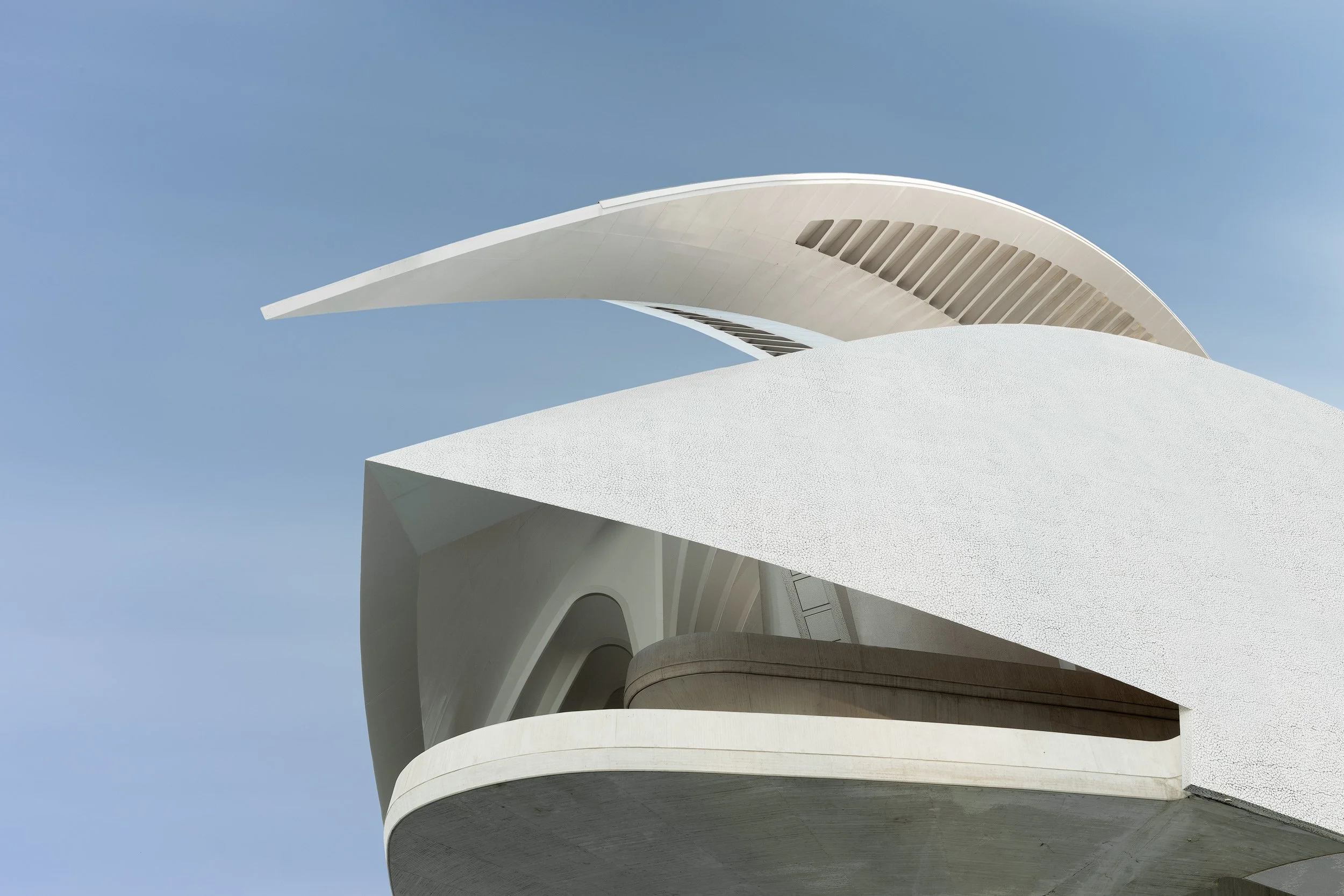 [architecture] [europe] [valencia] [colour] Palau de les Arts Reina Sofía Valencia by Calatrava, sweeping white crescent roof and layered concrete against blue sky. Architectural Photography by Jim Scott.