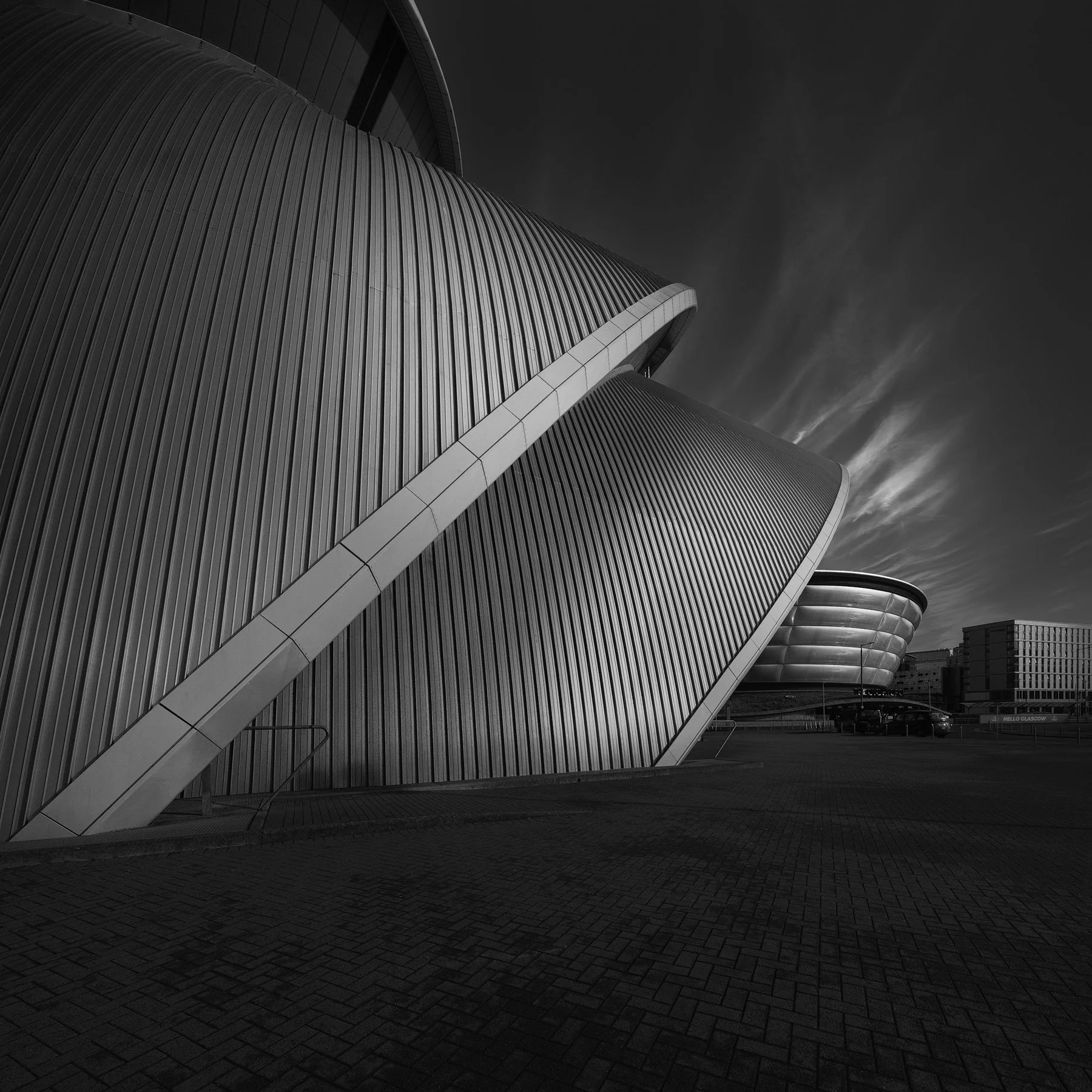 [architecture] [uk] [glasgow] [blackandwhite] [square] Armadillo Clyde Auditorium Glasgow up close, corrugated stainless steel shell cladding sweeping under dramatic clouds. Architectural Photography by Jim Scott.