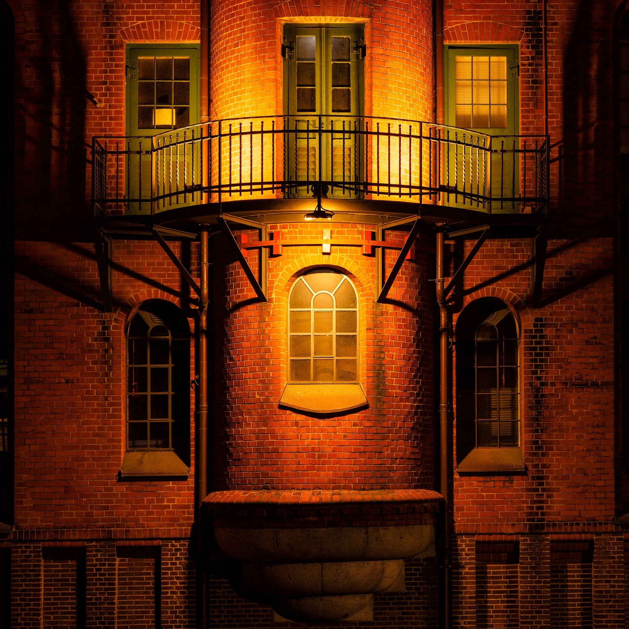 Historic industrial architecture in Hamburg, Germany: A dramatic study of the Speicherstadt warehouse district. This architectural photograph captures a symmetrical section of a traditional red-brick warehouse at night. The warm, artificial light fro