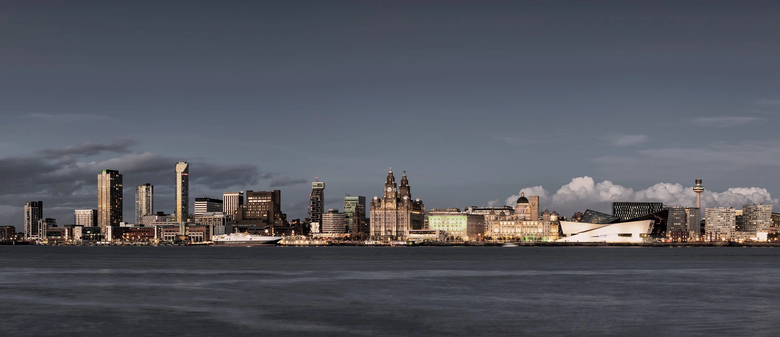 [architecture] [uk] [birkenhead] [colour] [panoramic] Dusk panorama of the Liverpool waterfront, Royal Liver Building and Museum of Liverpool reflected across the Mersey. Architectural Photography by Jim Scott.