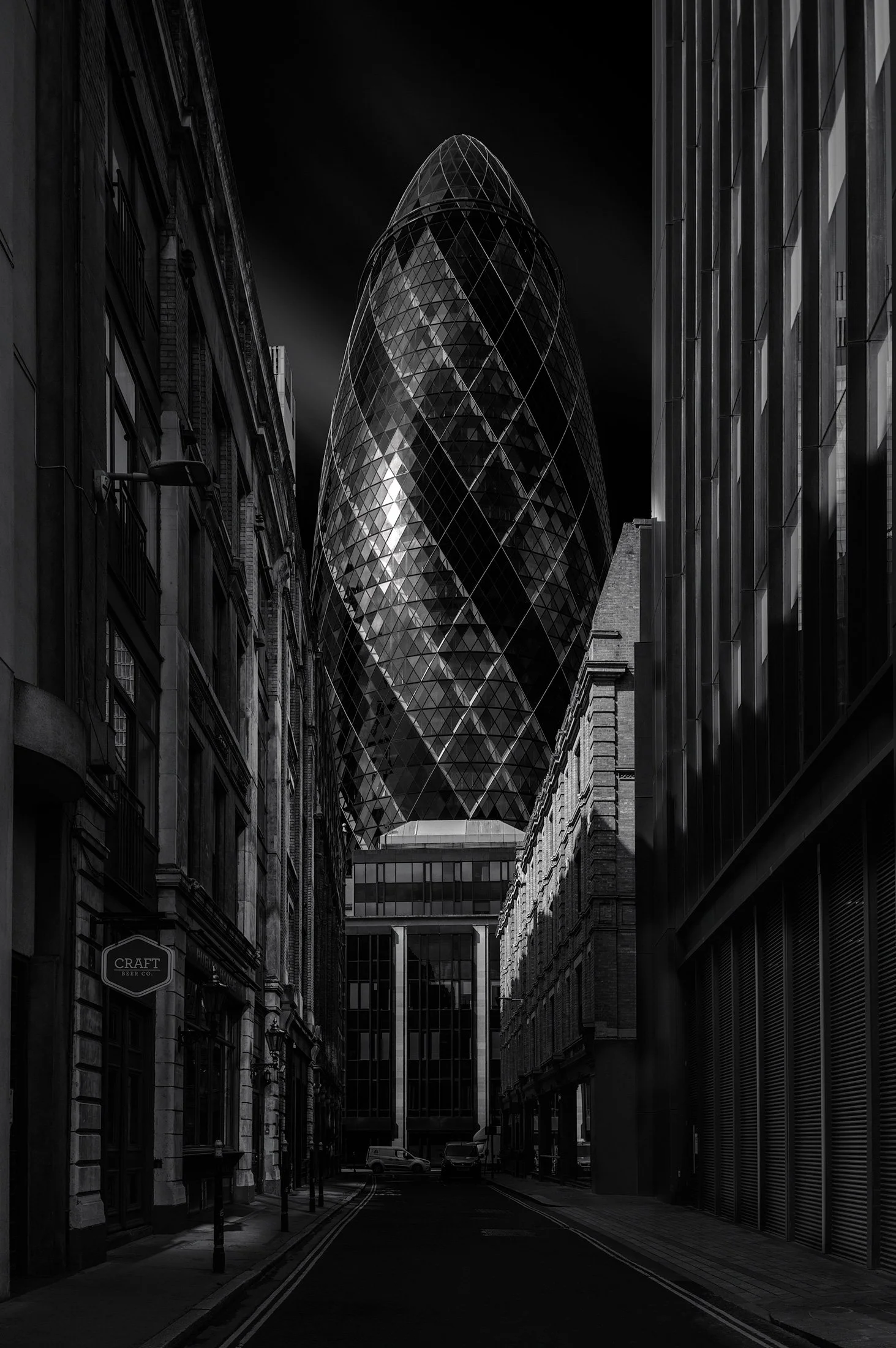 [architecture] [uk] [london] [blackandwhite] 30 St Mary Axe Gherkin London, framed at end of narrow Mitre Street canyon between Victorian and modern facades, moody long exposure. Architectural Photography by Jim Scott.