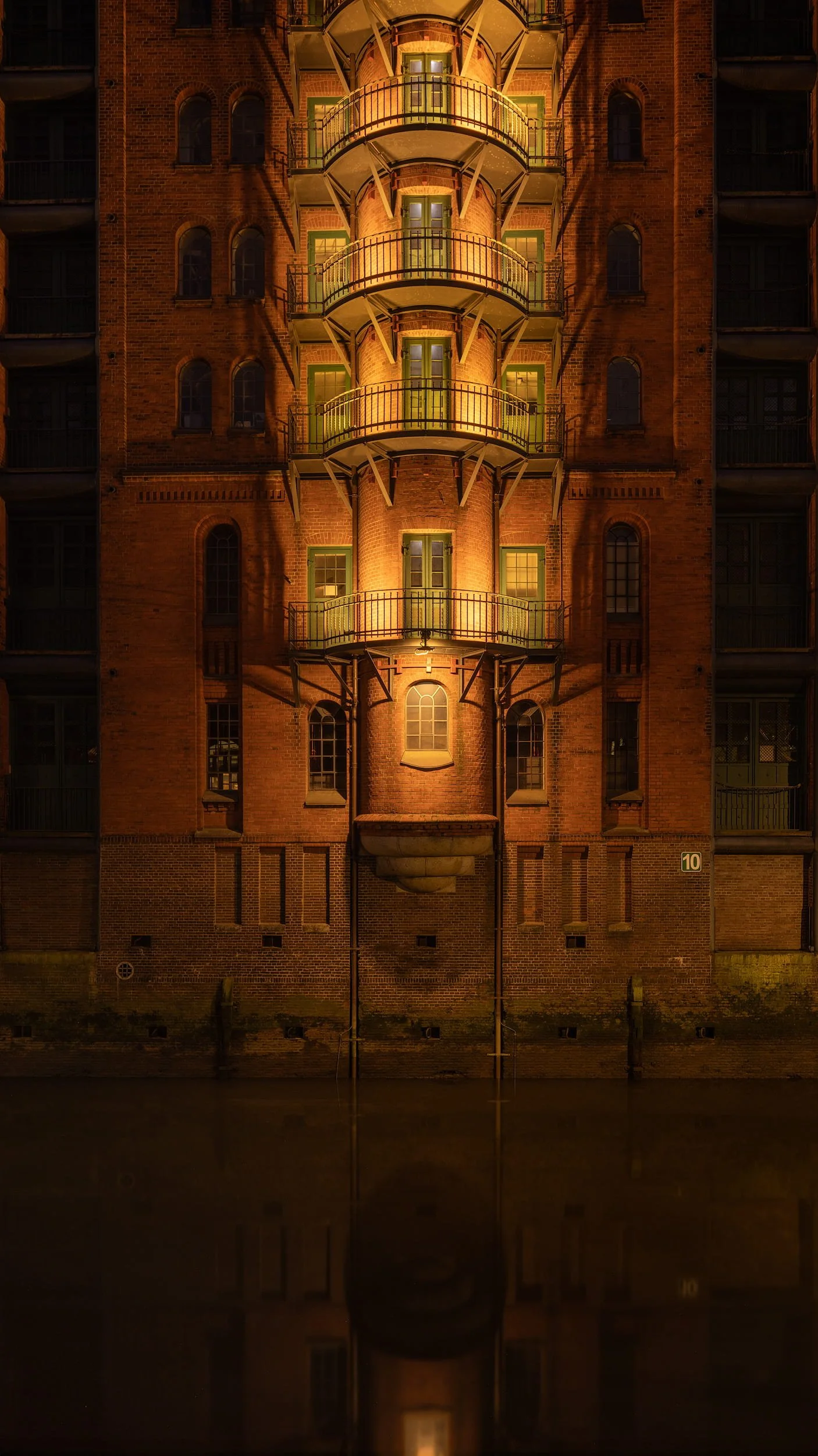 [architecture] [europe] [hamburg] [colour] [nightscape] Wasserschloss Speicherstadt Hamburg at night, illuminated curved balconies and arched windows reflected in the dark. Architectural Photography by Jim Scott.