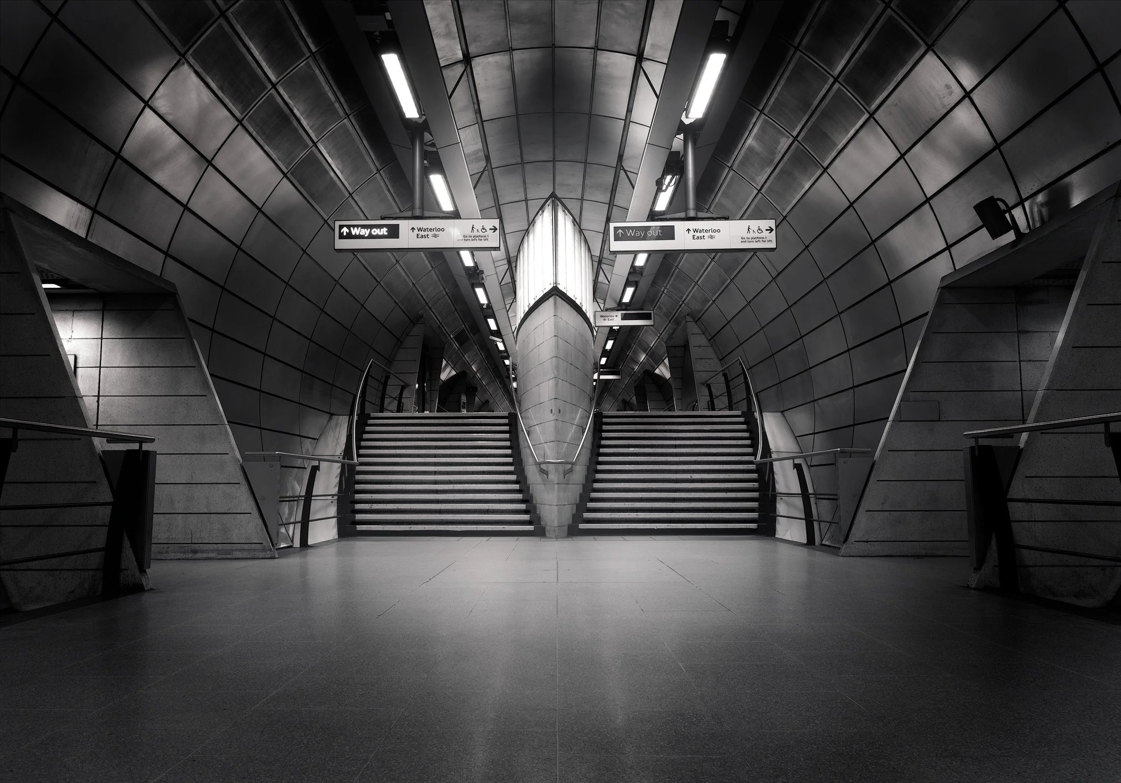 Contemporary transport architecture in London, UK: A dramatic monochromatic study of Southwark Underground station, designed by MacCormac Jamieson Prichard. This architectural photograph captures the symmetrical, twin staircases leading to the platfo