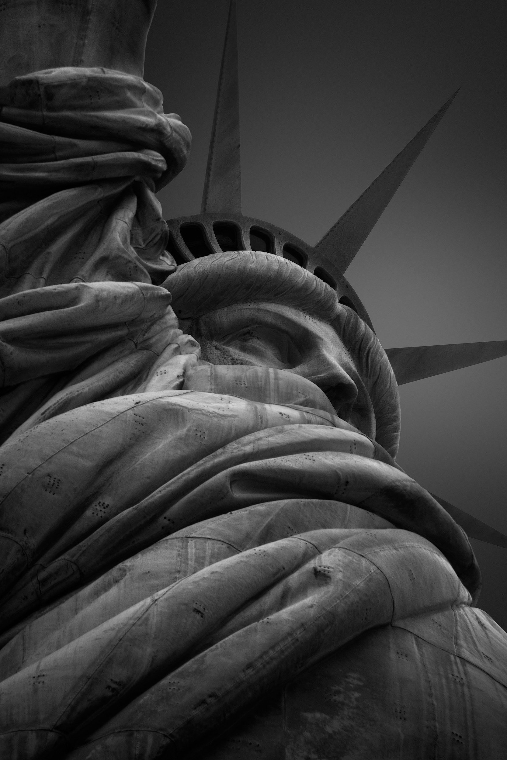 Iconic colossal sculpture in New York City: A dramatic monochromatic study of the Statue of Liberty, designed by Frédéric Auguste Bartholdi and engineered by Gustave Eiffel. This extreme low-angle photograph captures the dense textural detail of the 