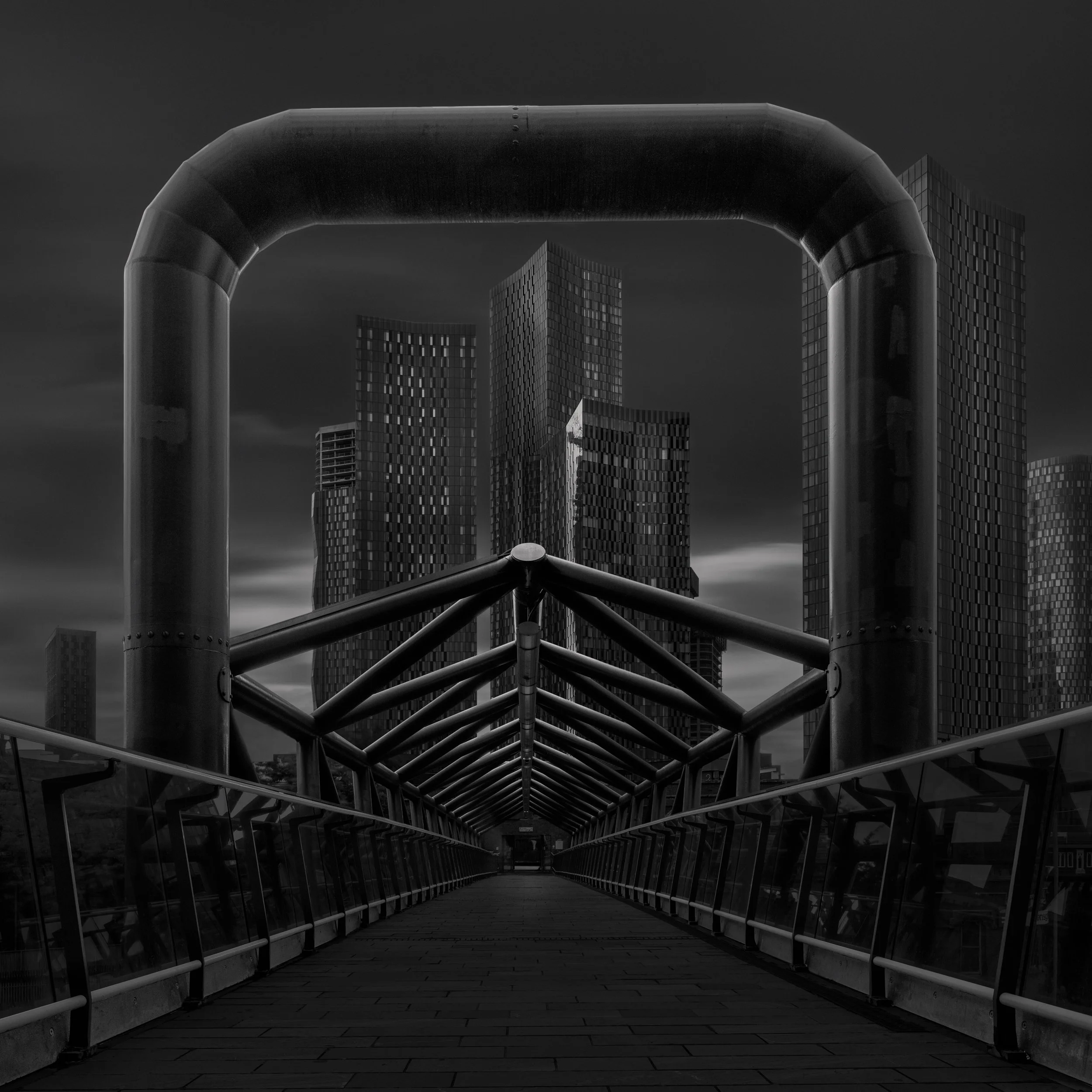 Contemporary urban transit in Manchester, UK: A symmetrical monochromatic study taken from the platform of Deansgate-Castlefield station. This architectural photograph captures the rhythmic repetition of the station’s modern steel supports, framing a
