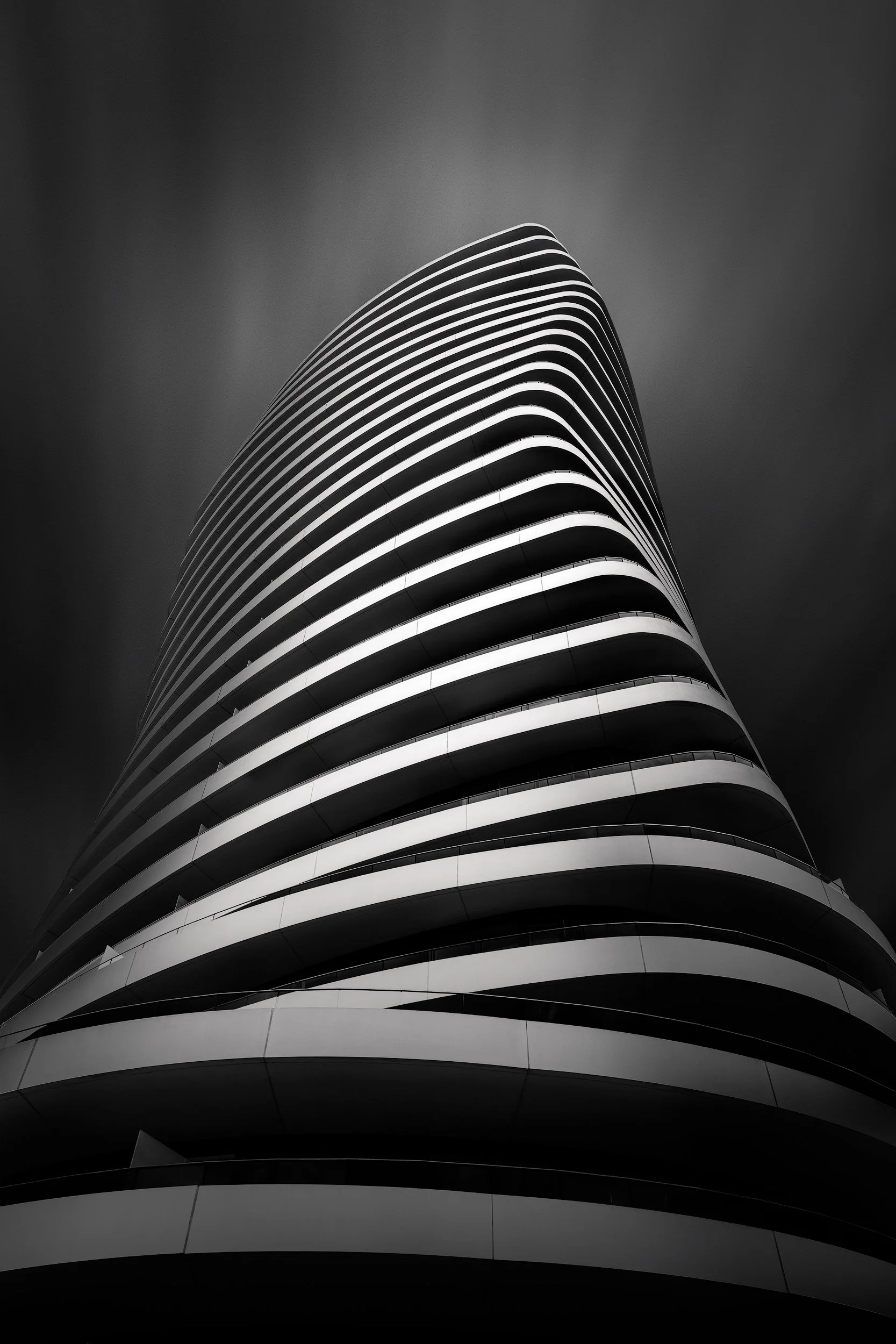 Contemporary residential architecture in Battersea, London: A dramatic monochromatic study of Lombard Wharf, designed by Patel Taylor. This architectural photograph captures the building’s distinctive plectrum-shaped footprint and its twisting, tiere