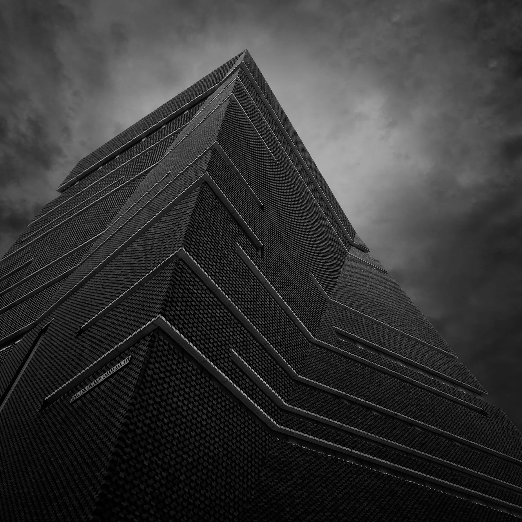[architecture] [uk] [london] [blackandwhite] [square] Tate Modern Blavatnik Building London upward abstract, dark lattice-brick pyramid corner rising under a brooding sky. Architectural Photography by Jim Scott.