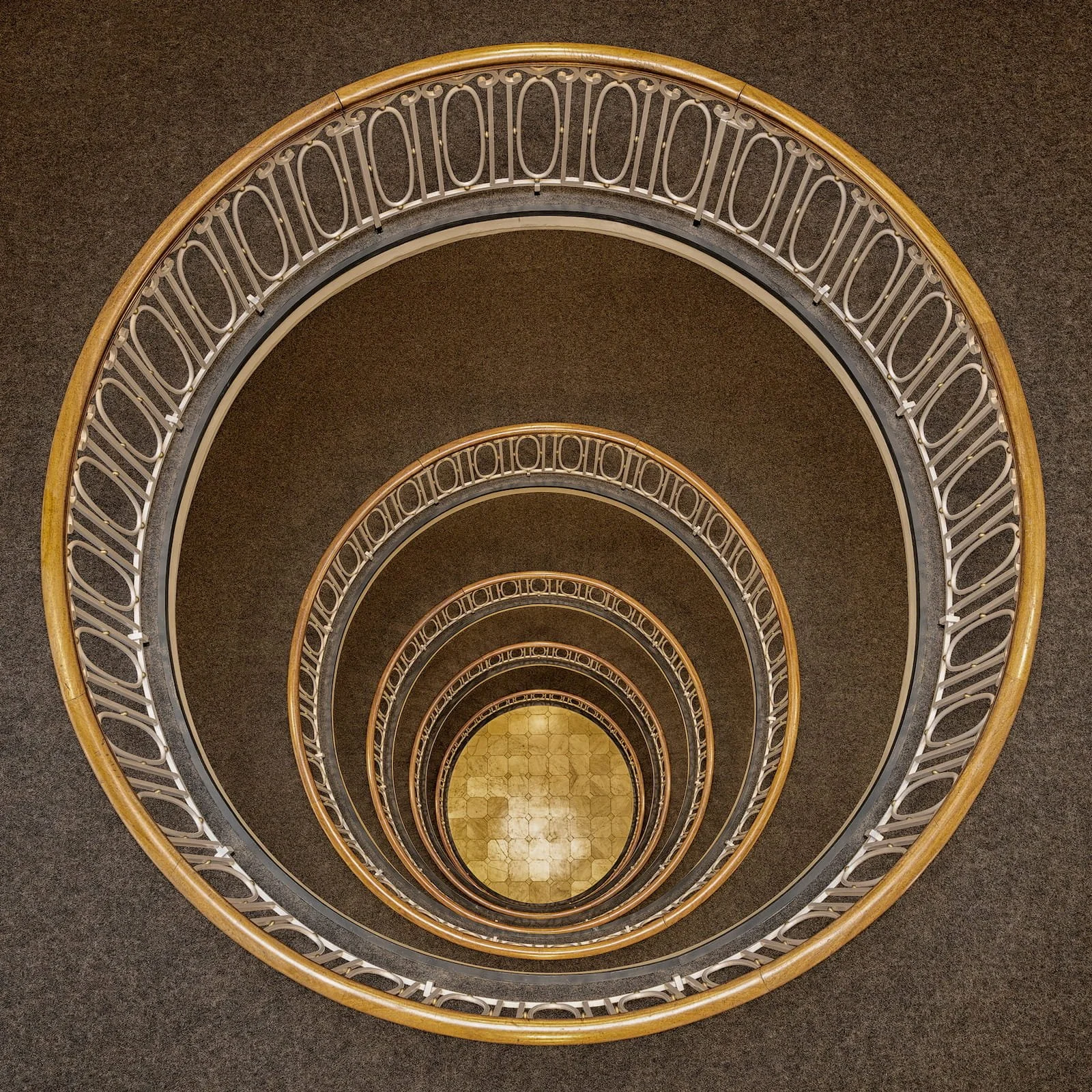 [architecture] [europe] [hamburg] [colour] [square] [internal] Esplanadebau Hamburg perfectly circular staircase from above, concentric golden handrail rings on warm tiled floor. Architectural Photography by Jim Scott.