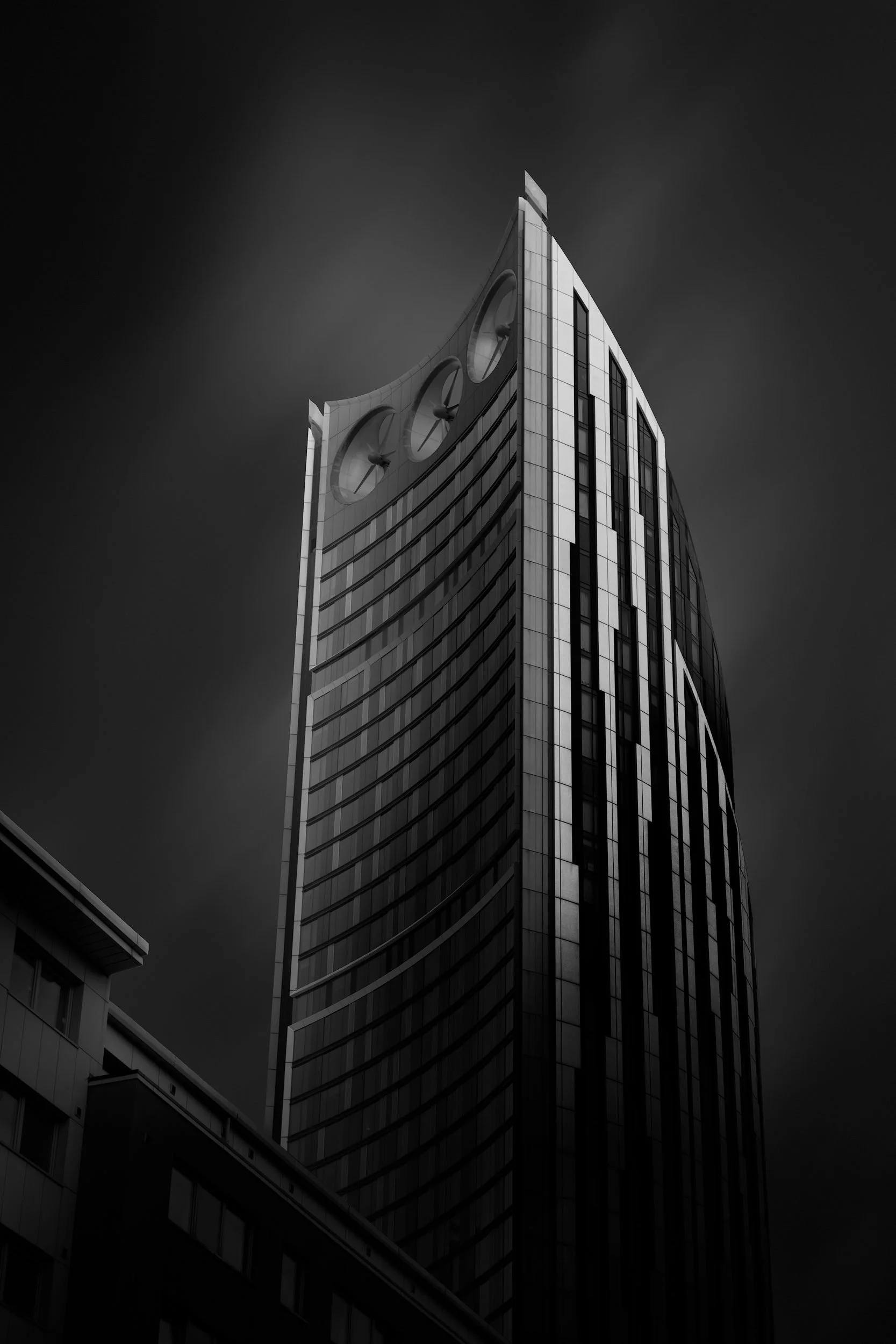 [architecture] [uk] [london] [blackandwhite] Strata SE1 Elephant and Castle London, curved concave top with three integrated wind turbine apertures under a dark sky. Architectural Photography by Jim Scott.
