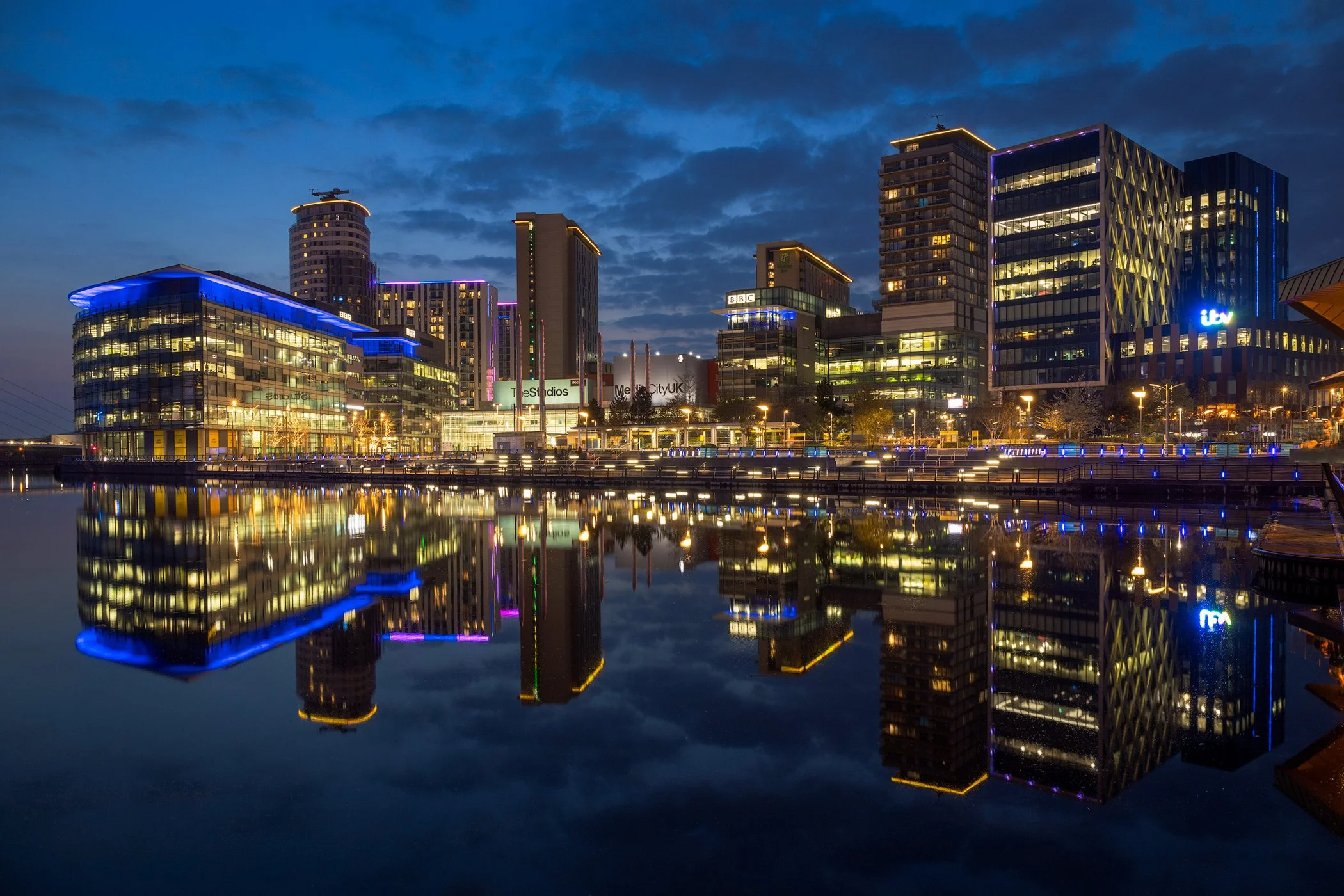 Contemporary urban regeneration at MediaCityUK, Salford Quays: A vibrant twilight long-exposure study of the Manchester Ship Canal waterfront. This cityscape photograph captures the illuminated headquarters of the BBC and ITV reflected in the still w