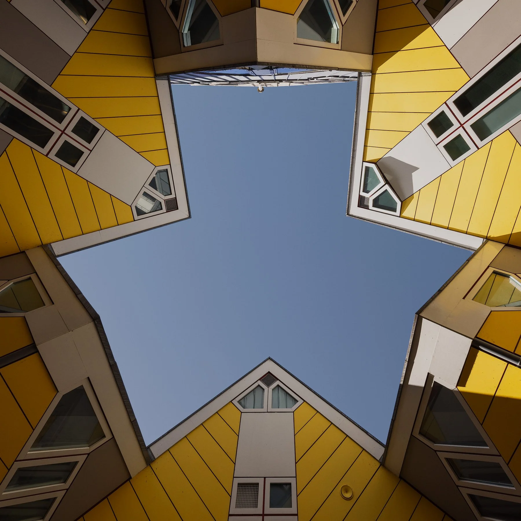 [architecture] [europe] [rotterdam] [colour] [square] Cube Houses Rotterdam upward in colour, Piet Blom's tilted yellow cubic homes forming a star-shaped void of blue sky. Architectural Photography by Jim Scott.