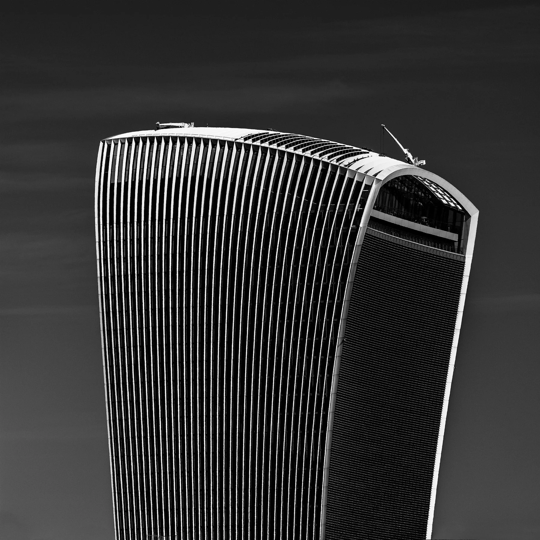 Black and white photo of a modern, curved skyscraper under a dark sky, with a crane on top.