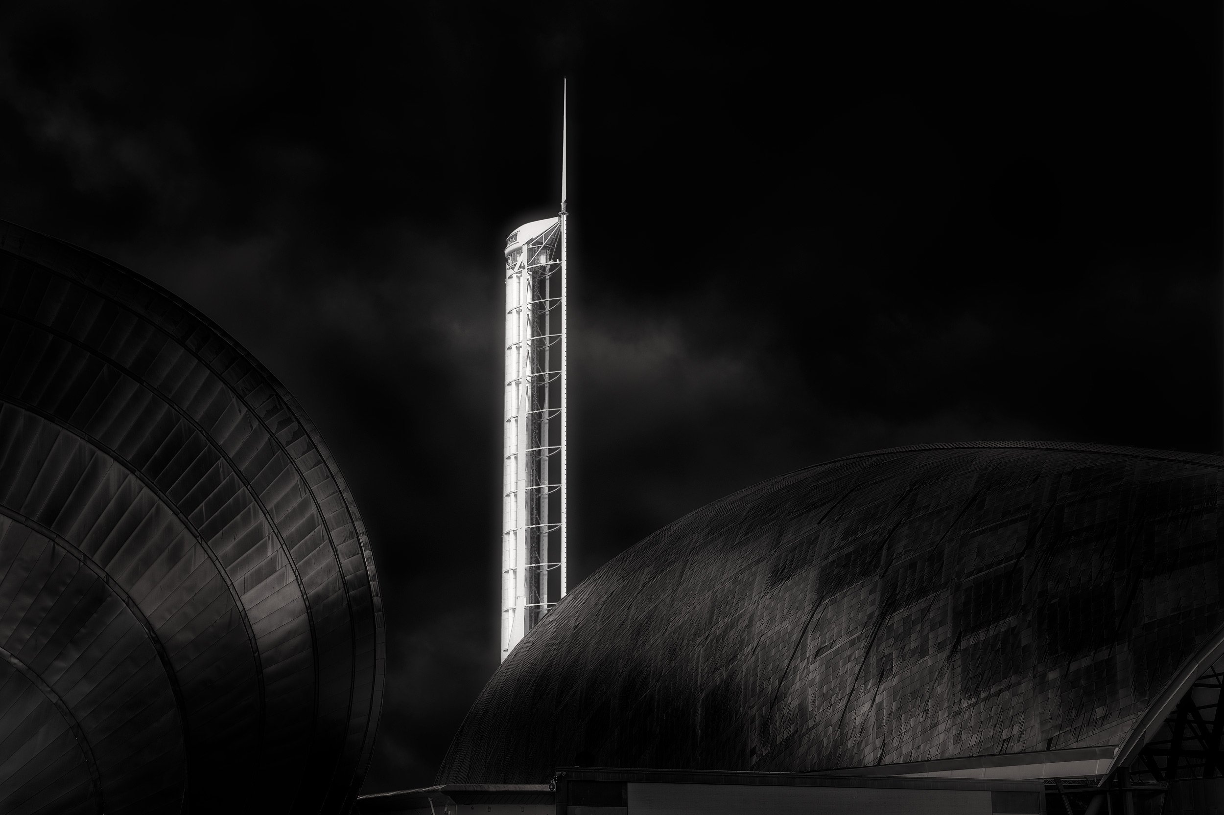 Contemporary architectural landmarks in Glasgow, Scotland: A dramatic monochromatic study of the Glasgow Science Centre Tower and the IMAX theatre. This high-contrast photograph captures the world’s tallest rotating tower as a glowing monolith, frame