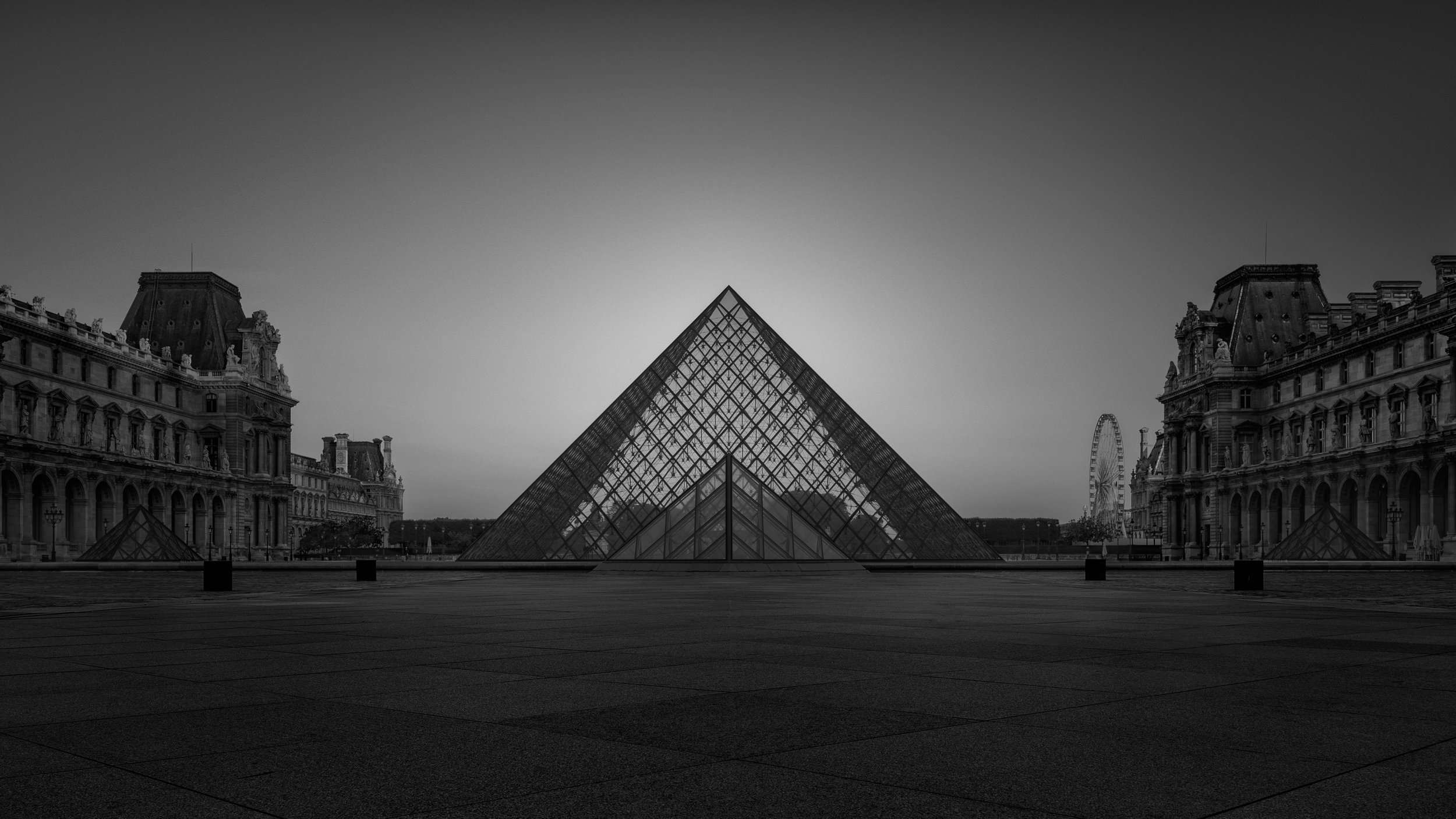 Modernist architecture at the Louvre Museum, Paris: A symmetrical monochromatic study of the Louvre Pyramid, designed by I. M. Pei. This architectural photograph utilises a long-exposure technique to isolate the glass structure within an empty Cour N