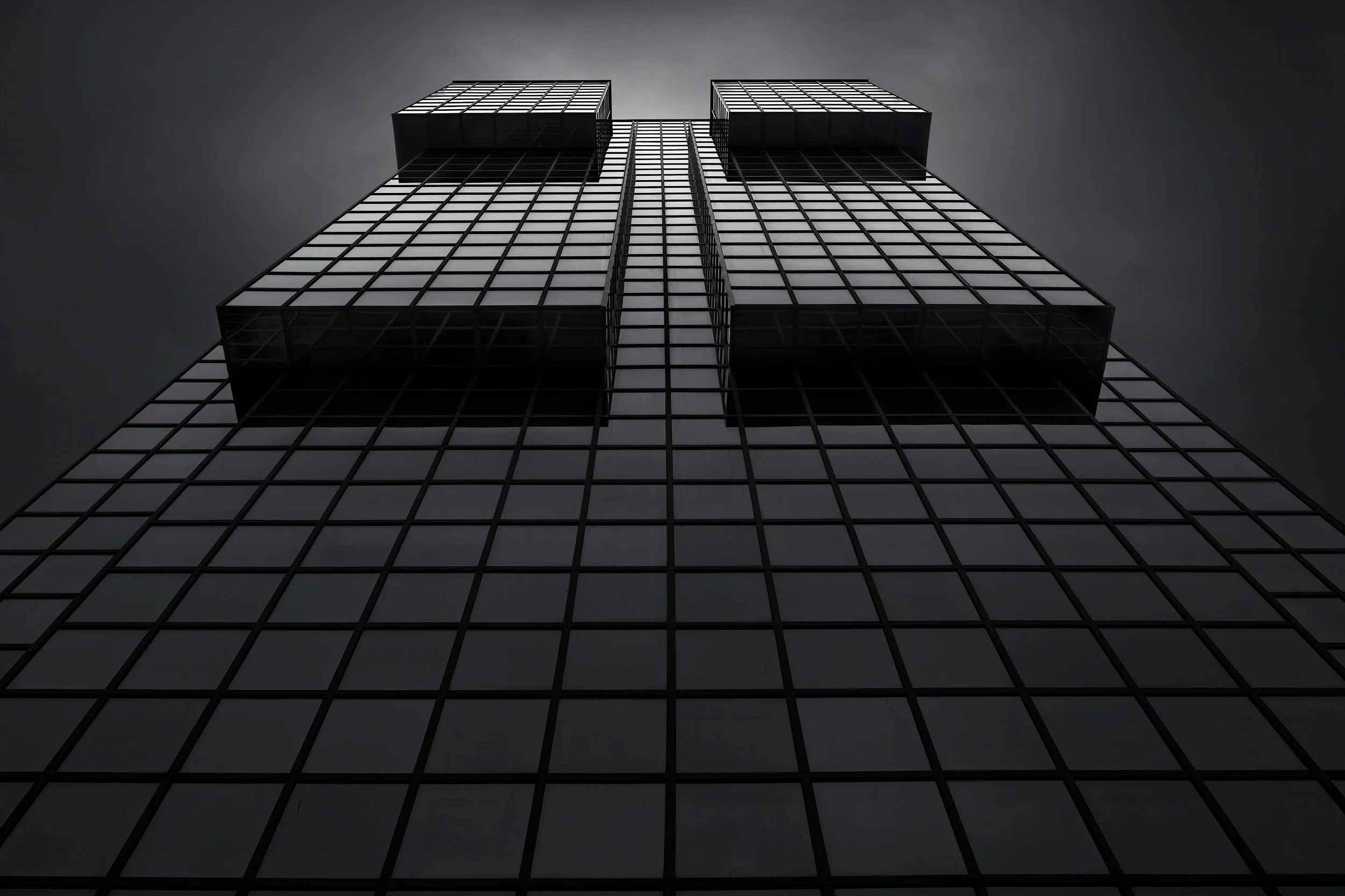 [architecture] [uk] [london] [blackandwhite] Northern Shell London from below, dark glass curtain wall split into two stepped slab forms against a cool grey sky. Architectural Photography by Jim Scott.